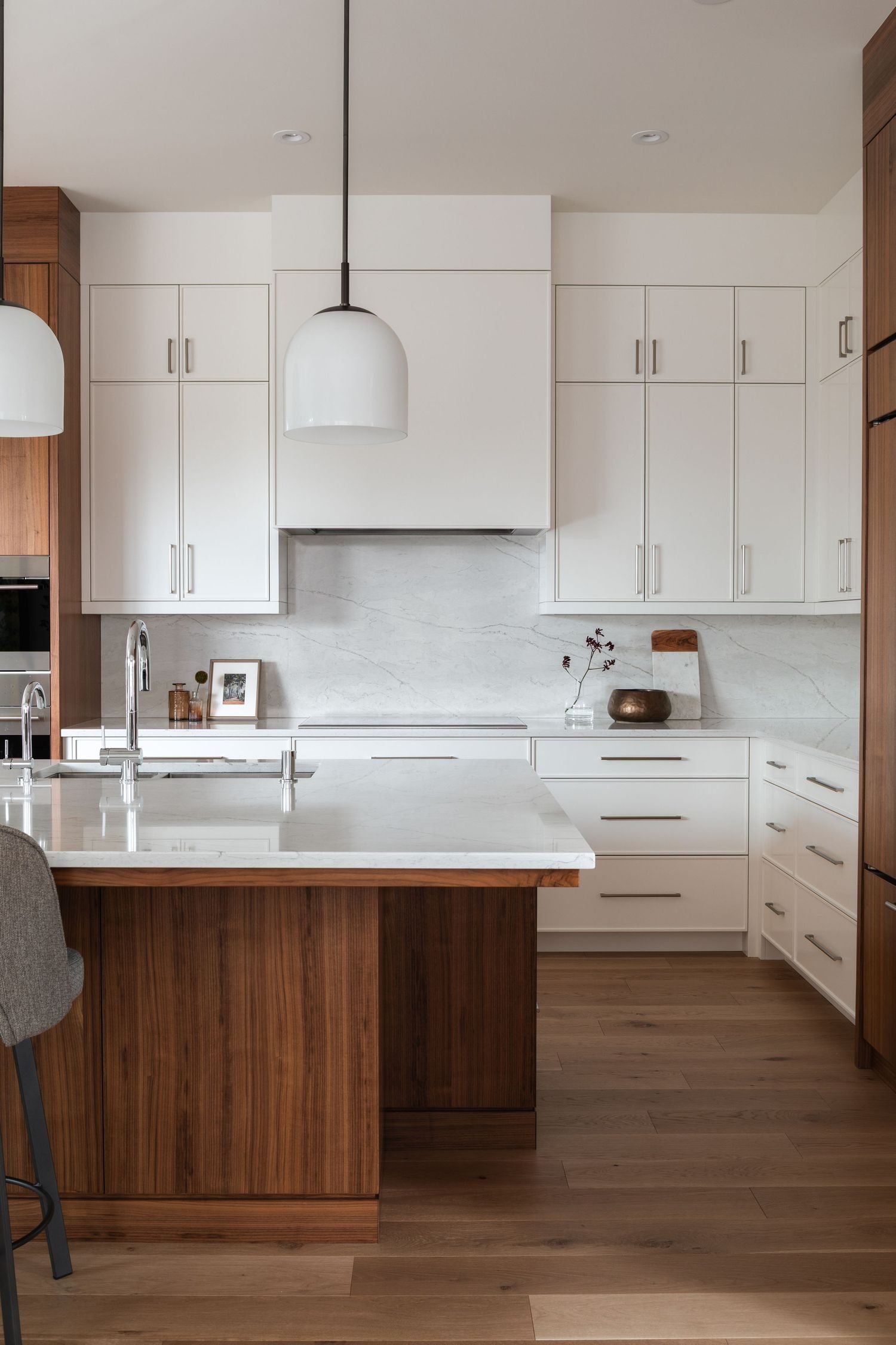 Contemporary kitchen featuring white upper cabinets, walnut island, marble backsplash, quartz countertops, and pendant lighting.