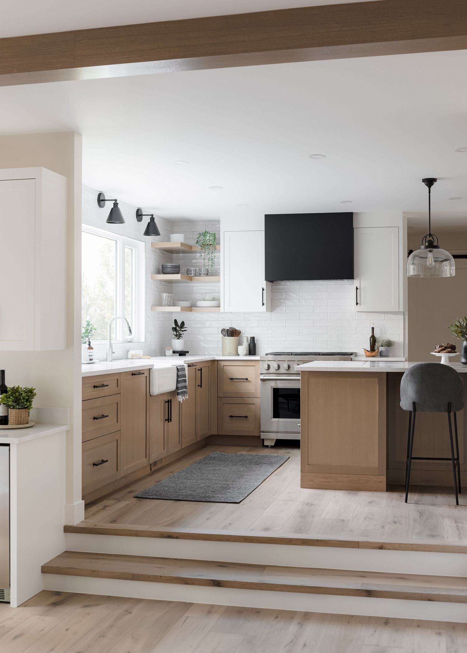 Bright open-concept kitchen featuring warm wood cabinets, black range hood, open shelving, farmhouse sink, and light hardwood floors.