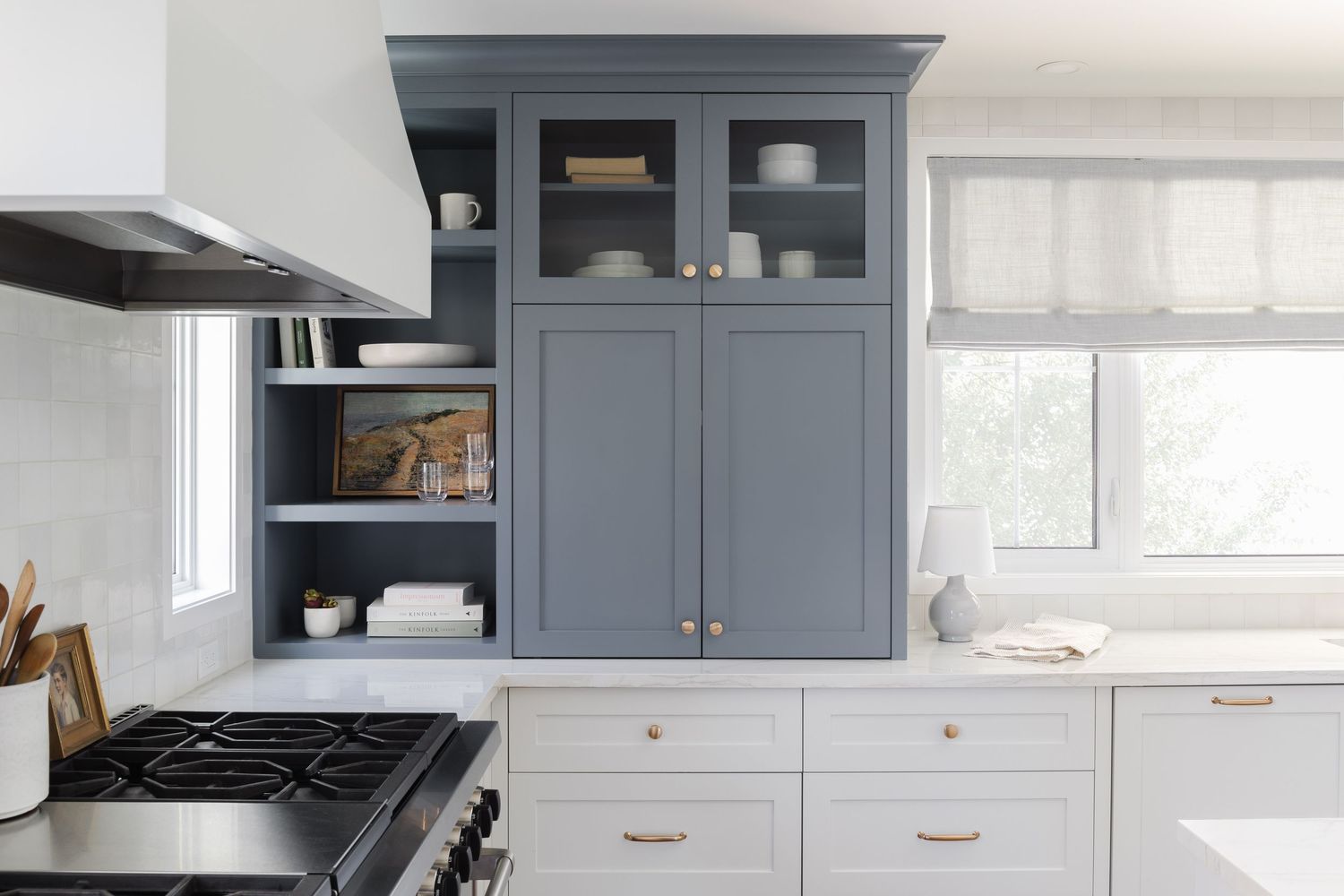 Blue-gray shaker kitchen cabinets with glass doors, open shelving, and white lower cabinets with copper pulls.