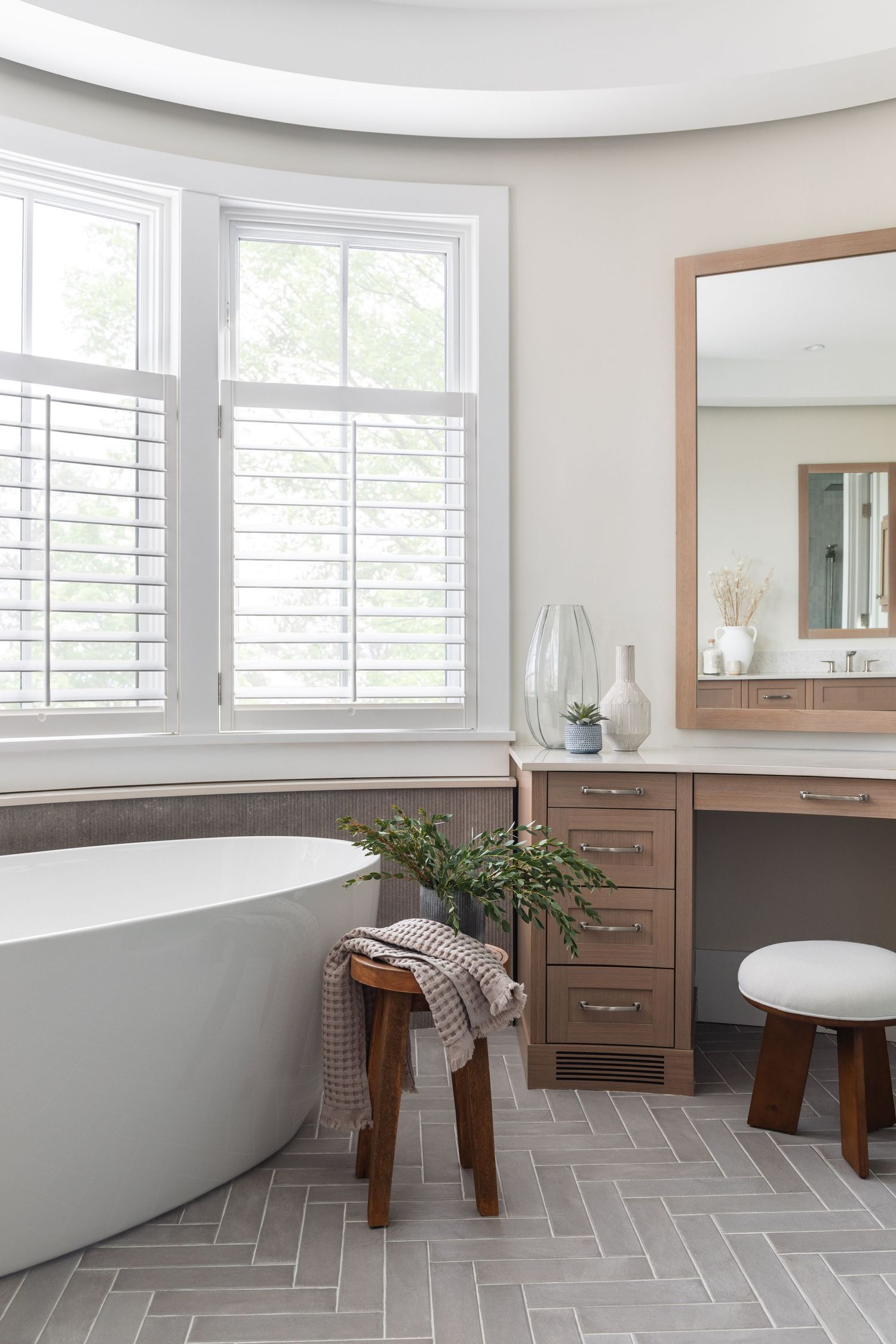 Spa-like bathroom with freestanding soaking tub, herringbone tile floor, and warm wood vanity.