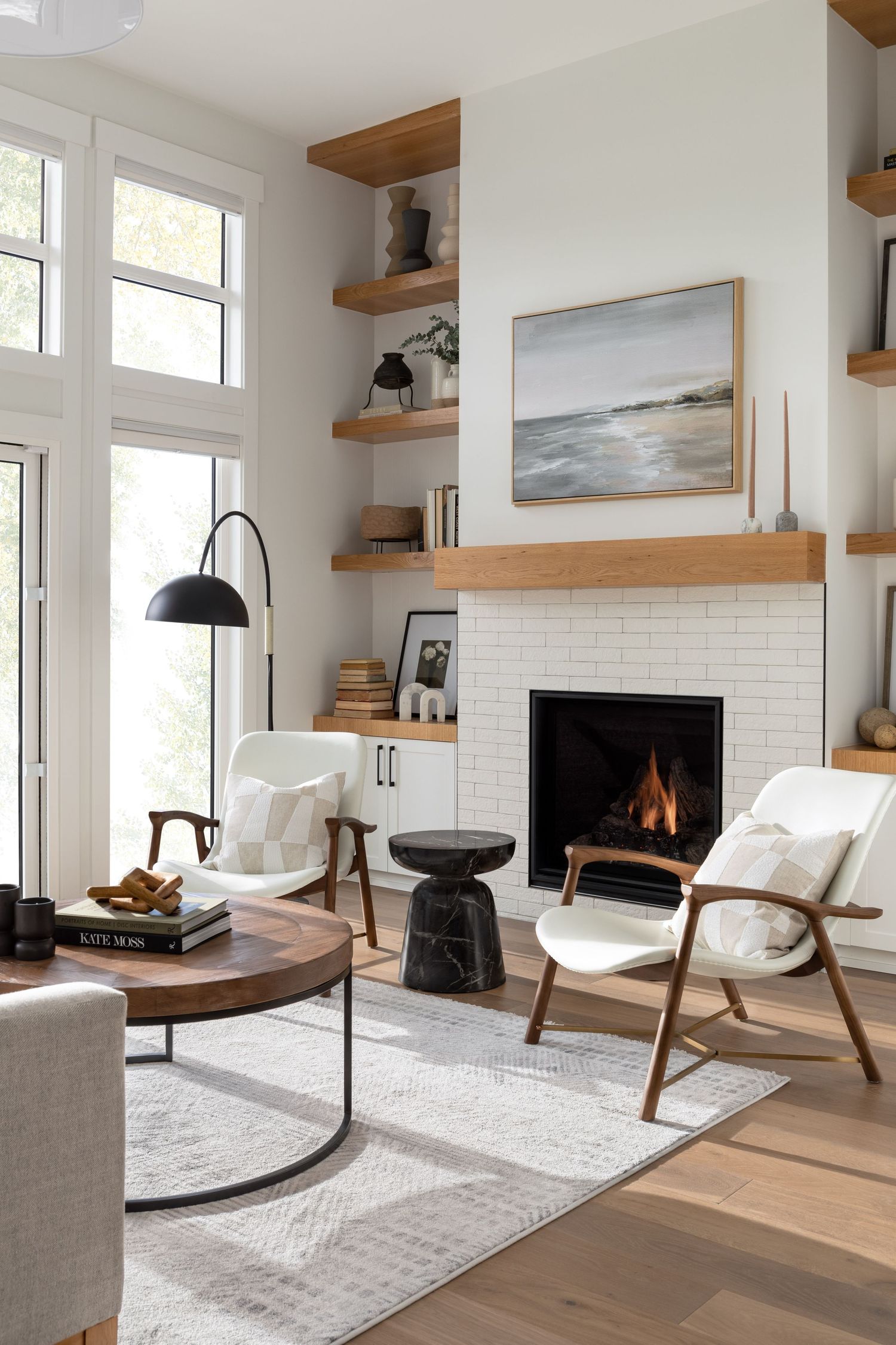 Scandinavian living room with white brick fireplace, oak shelving, white chairs, and wood accents.