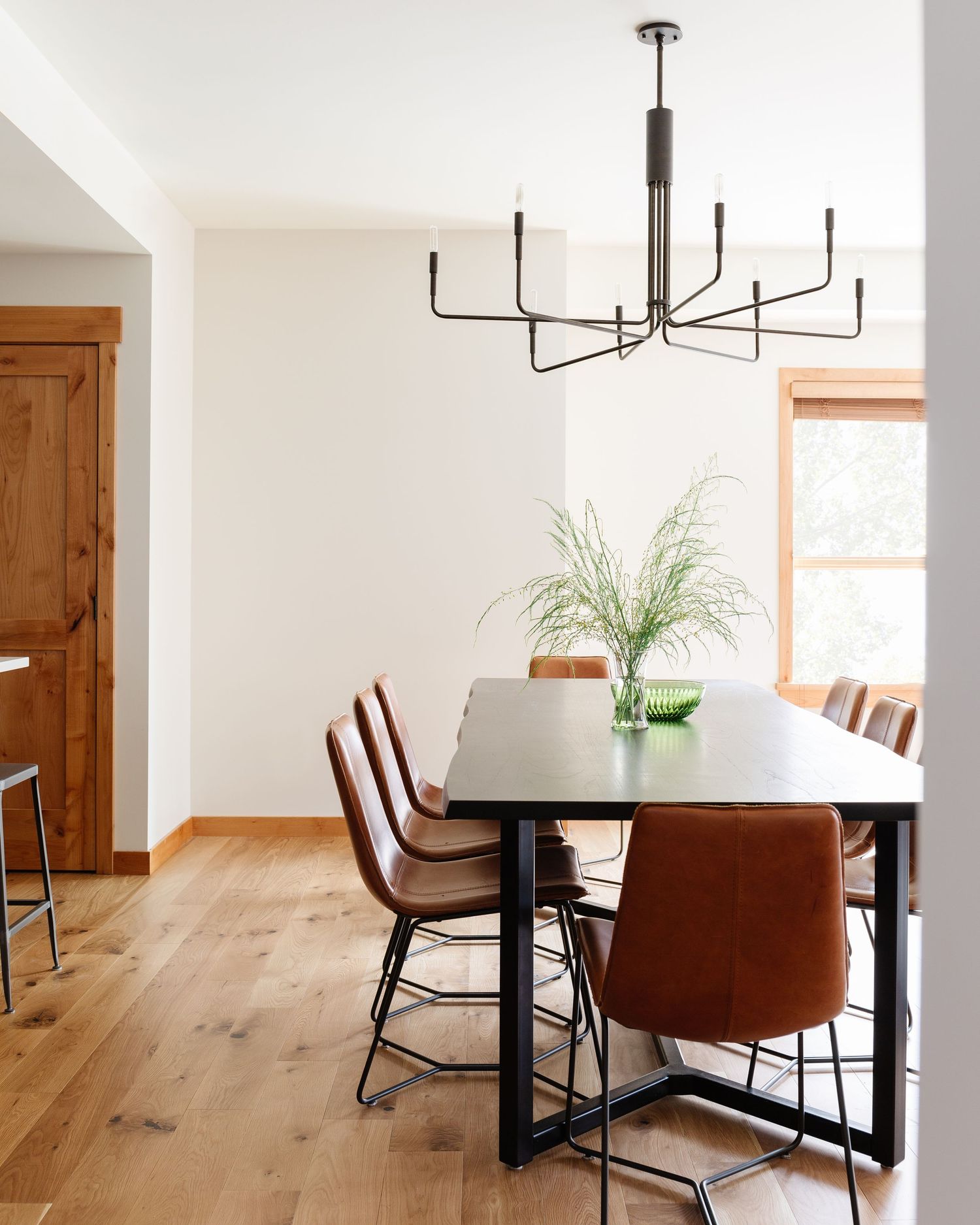 Modern dining room with black table, cognac leather chairs, multi-arm chandelier, and warm wood floors.