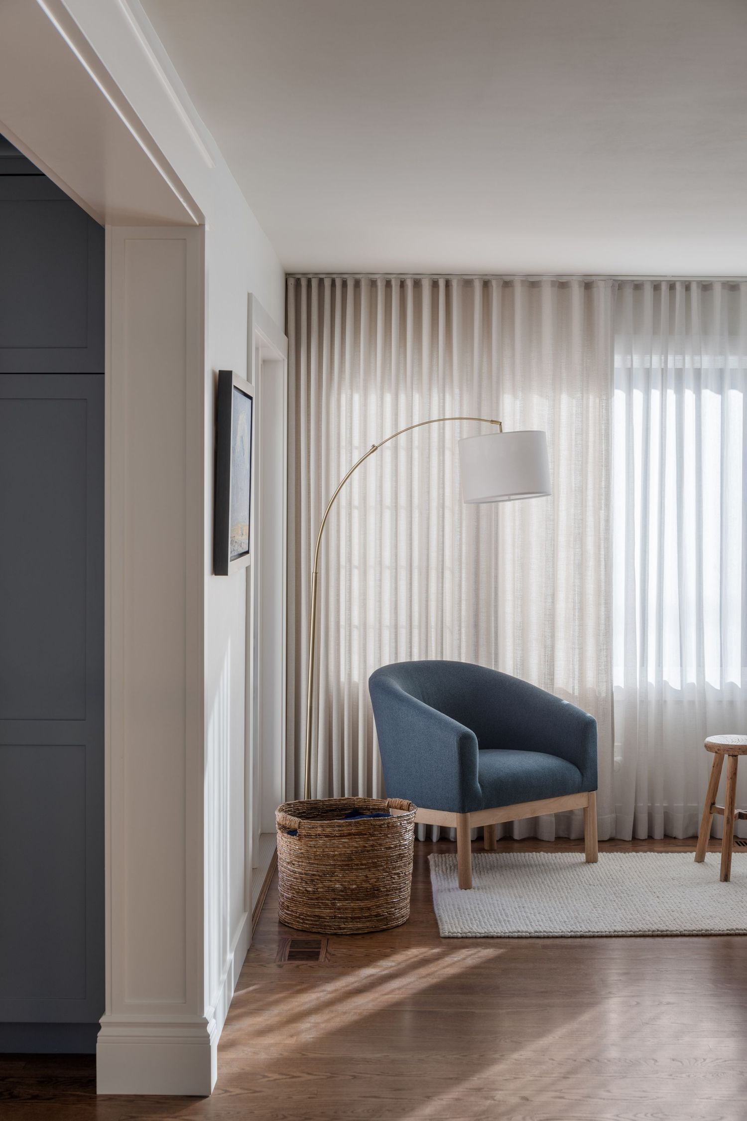 Cozy reading nook with blue barrel chair, arc floor lamp, woven basket, and sheer floor-to-ceiling curtains.