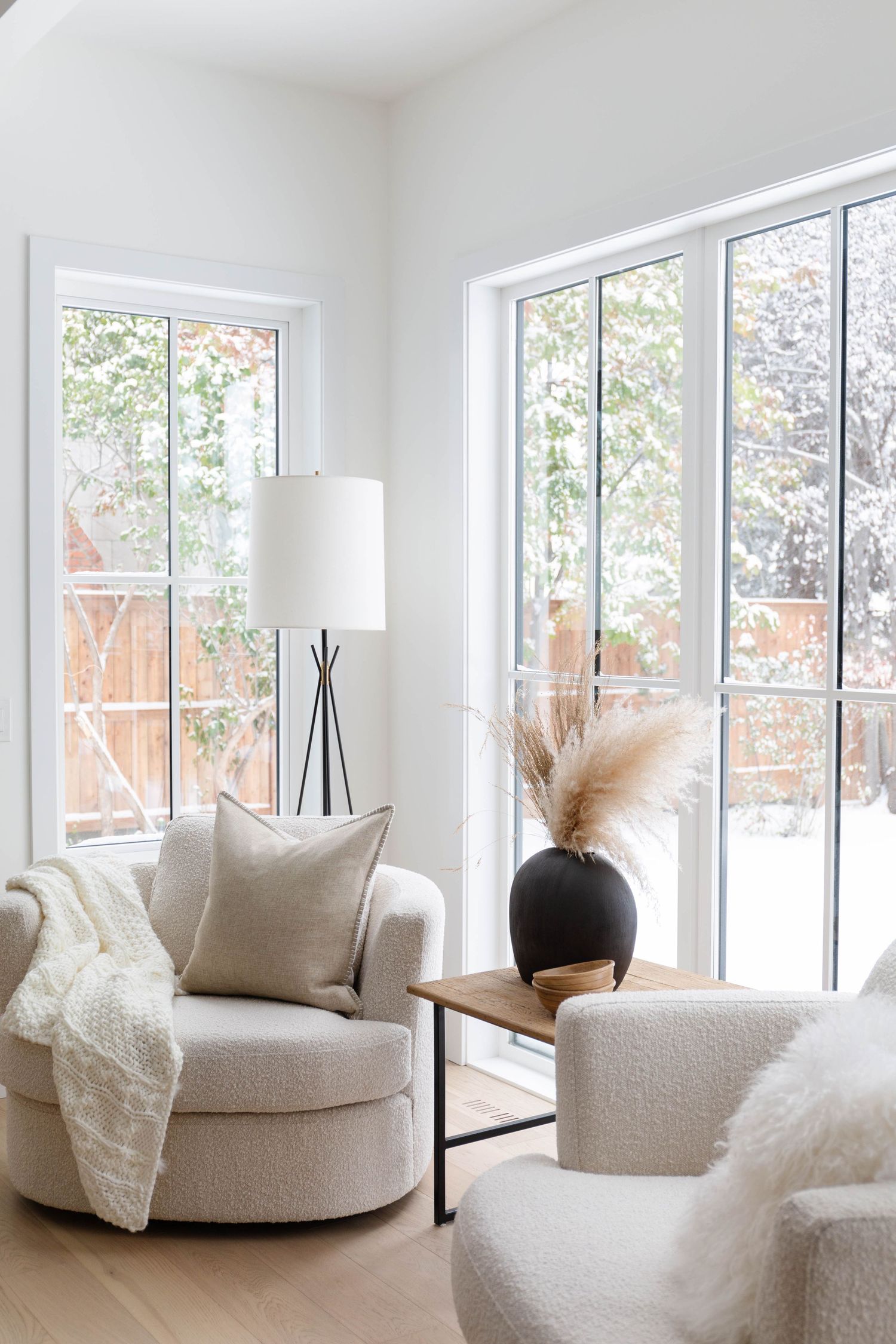 Bright minimalist sitting room with round chairs, black floor lamp, and large windows.