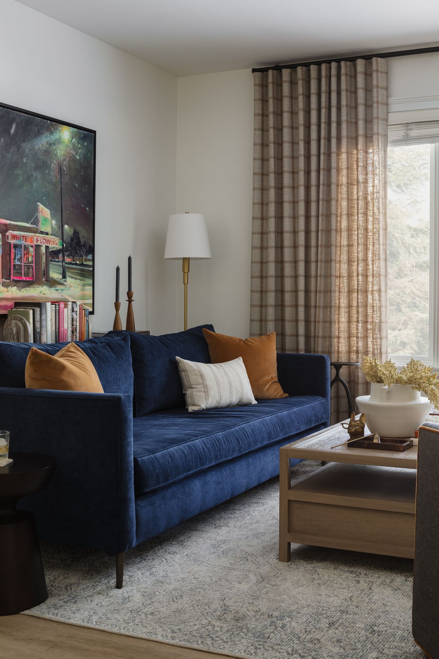 Warm living room with navy velvet sofa, amber cushions, plaid curtains, and large colorful wall art.