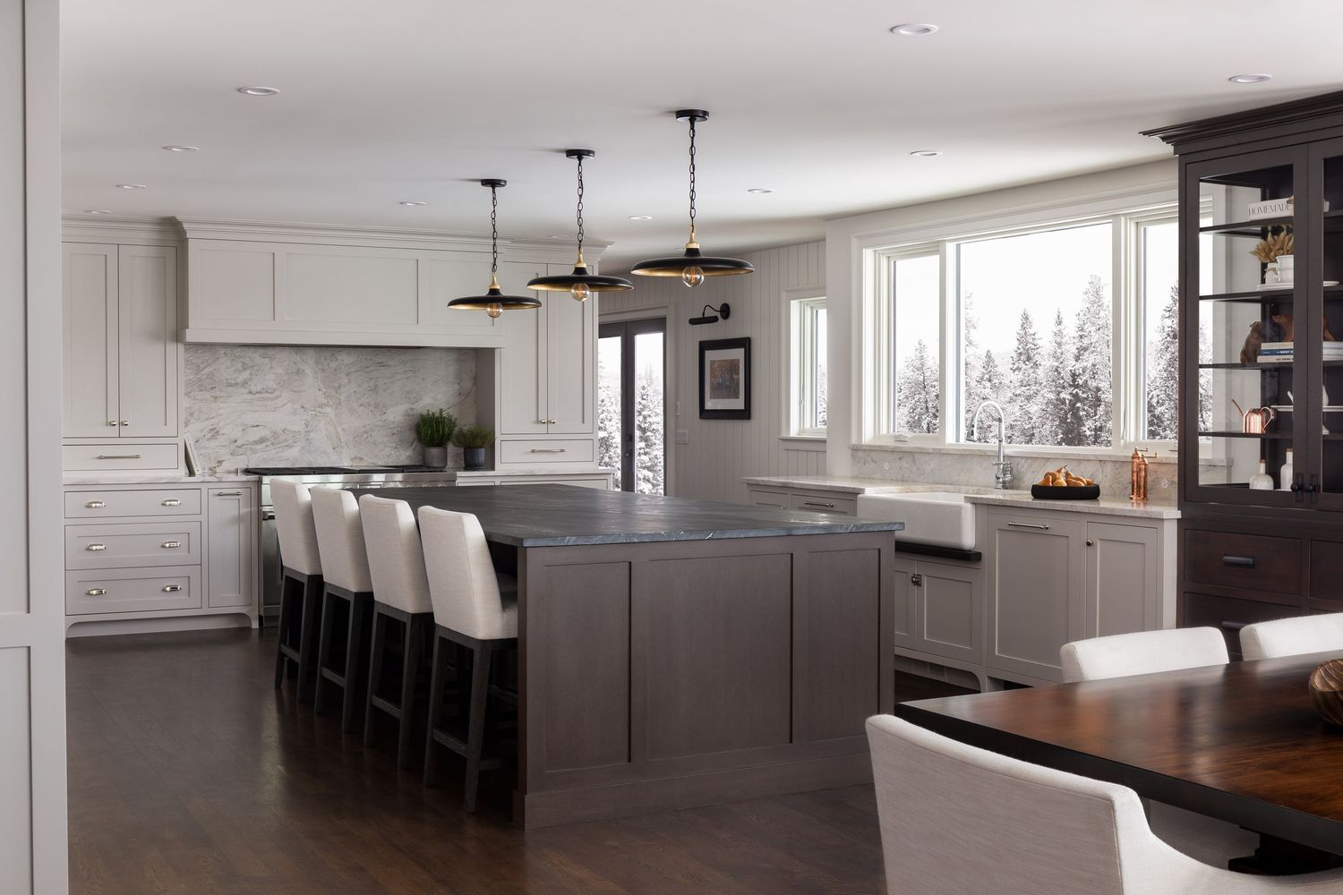 White kitchen with gray island, black barstools, marble backsplash, dark wood floors, and black pendant lights.