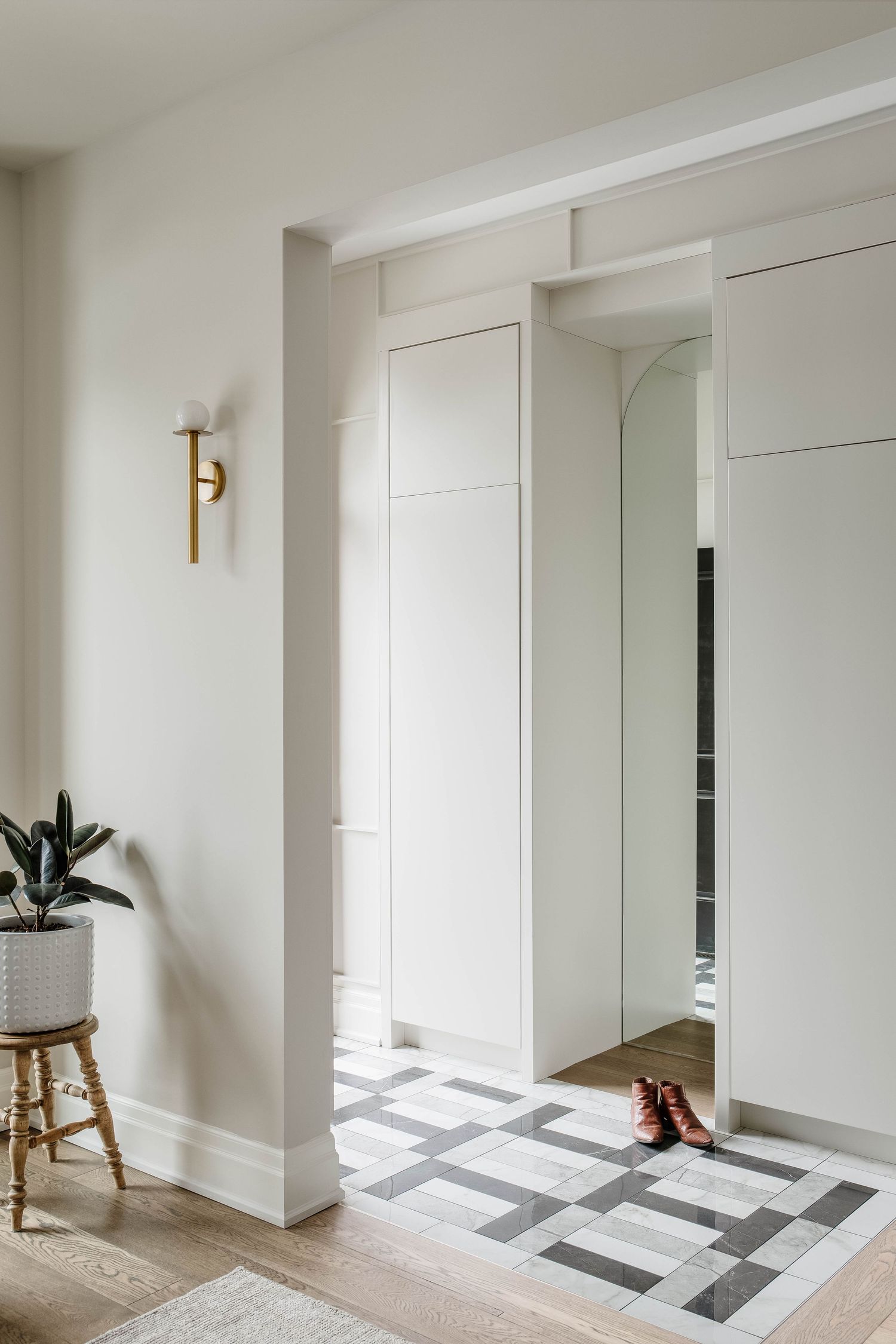 Bright entryway with white built-in cabinets, brass wall sconce, geometric tile floor, and arched mirror detail.