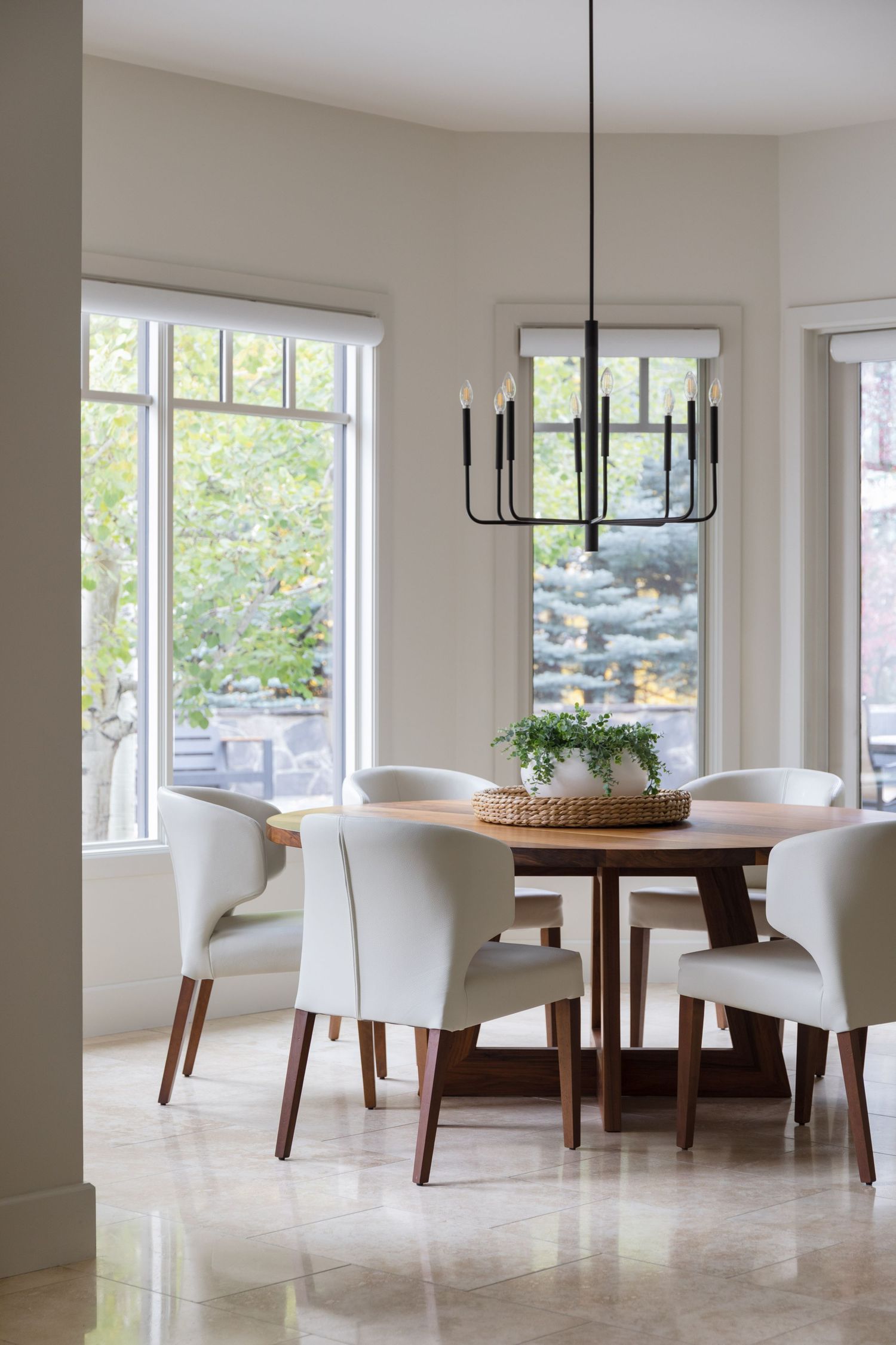 Bright dining room with round wood table, white upholstered chairs, and black candle chandelier.