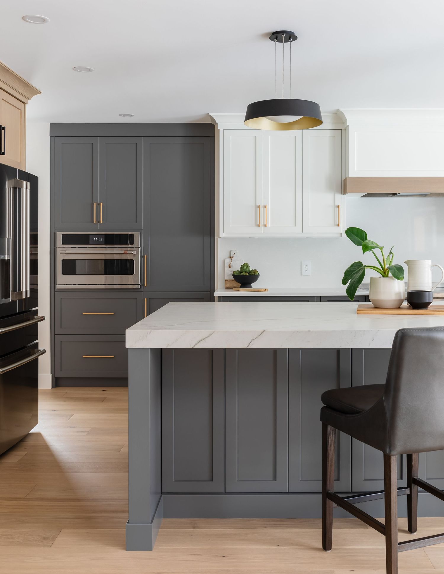Gray and white two-tone kitchen with marble island, gold pulls, and black pendant light.