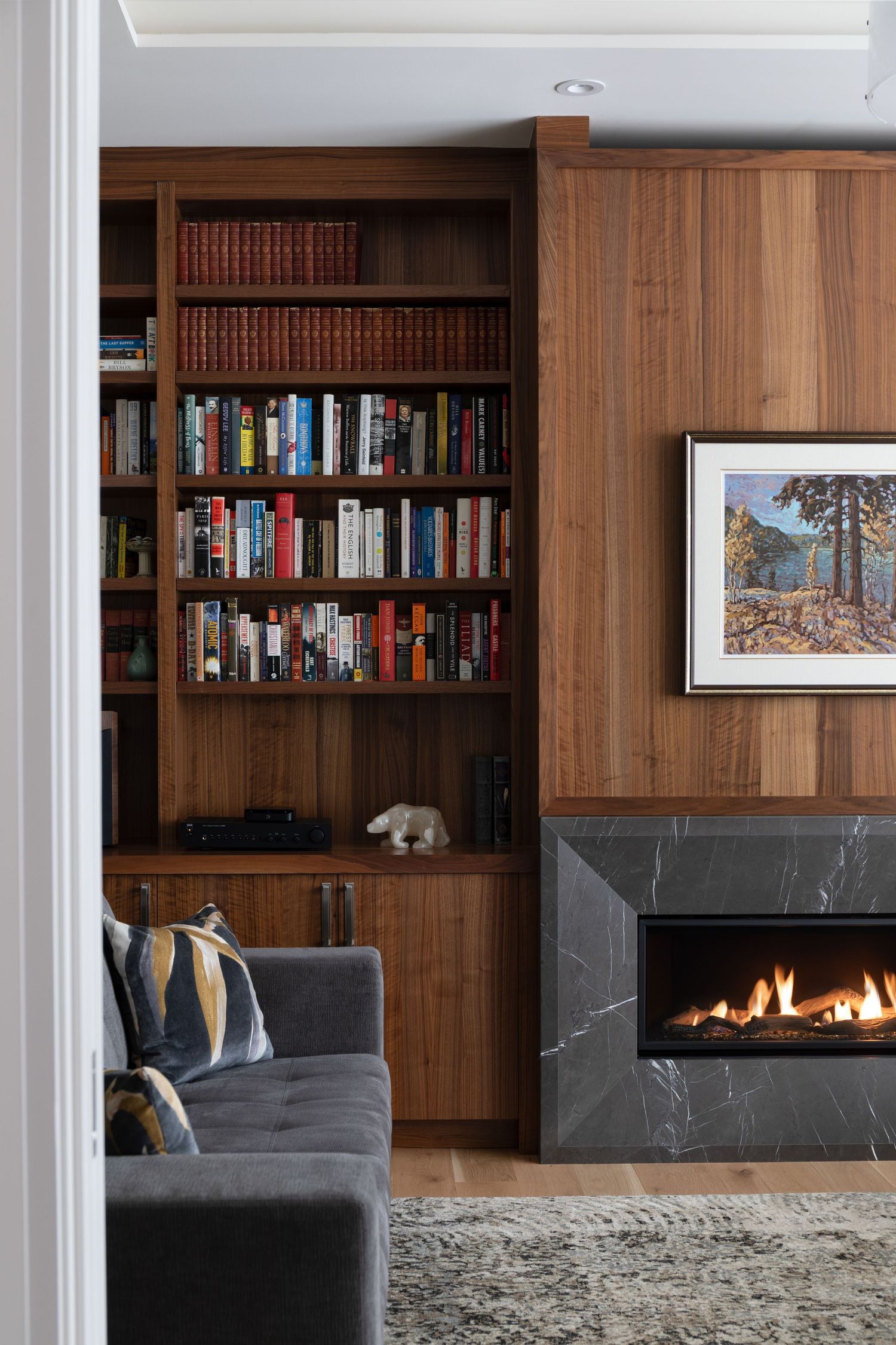Sophisticated living room with floor-to-ceiling walnut built-ins, marble linear fireplace, gray sofa, and colorful artwork.
