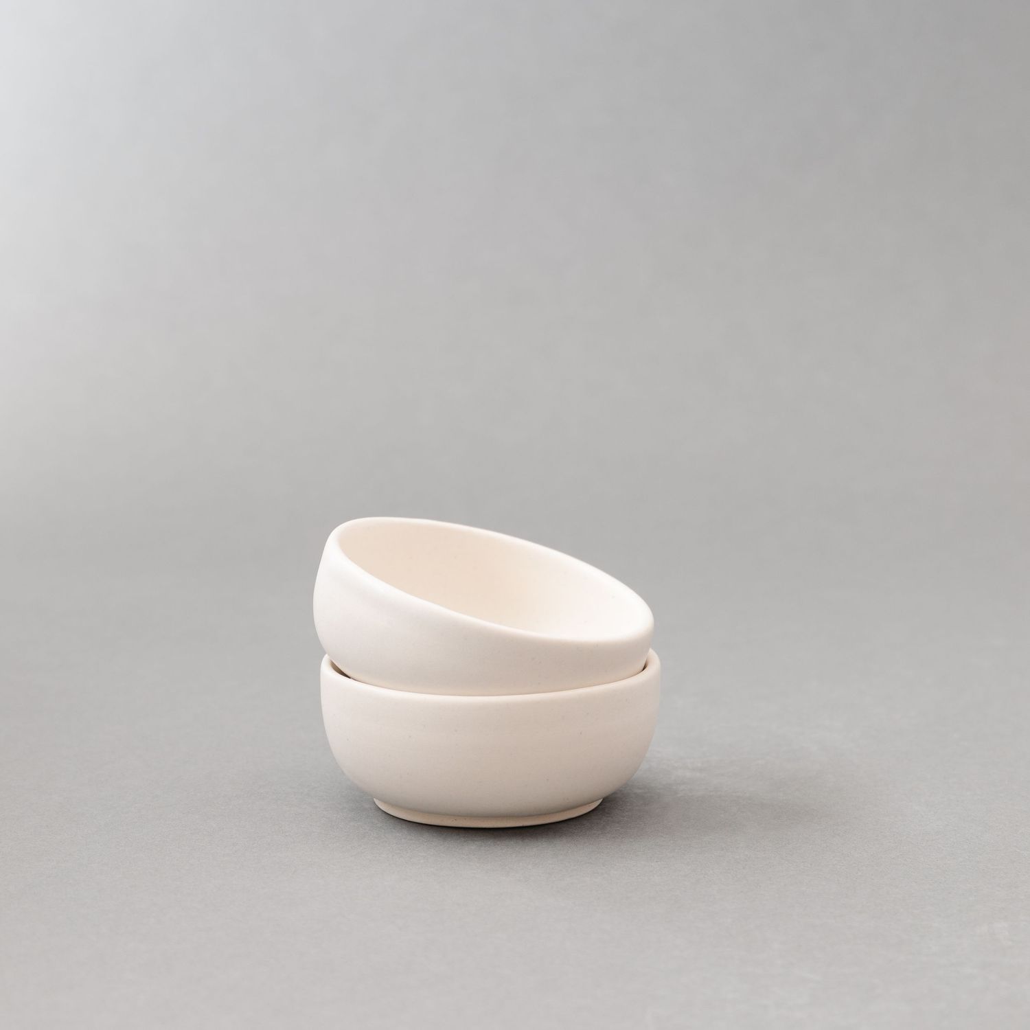 Two stacked minimalist white ceramic bowls with matte finish, modern Scandinavian style pottery tableware.