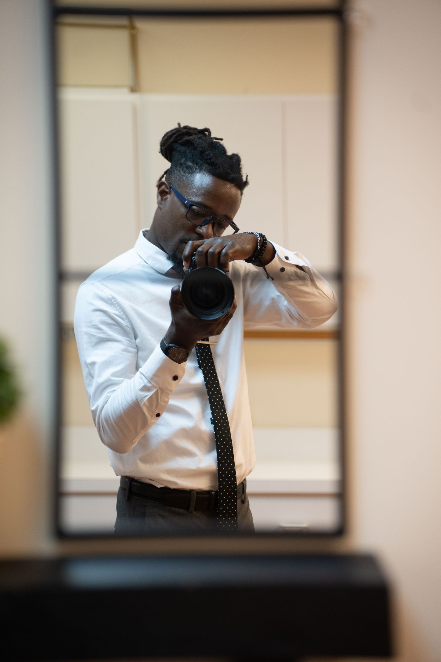 Professional photographer in formal attire takes a photo with DSLR camera in office setting.