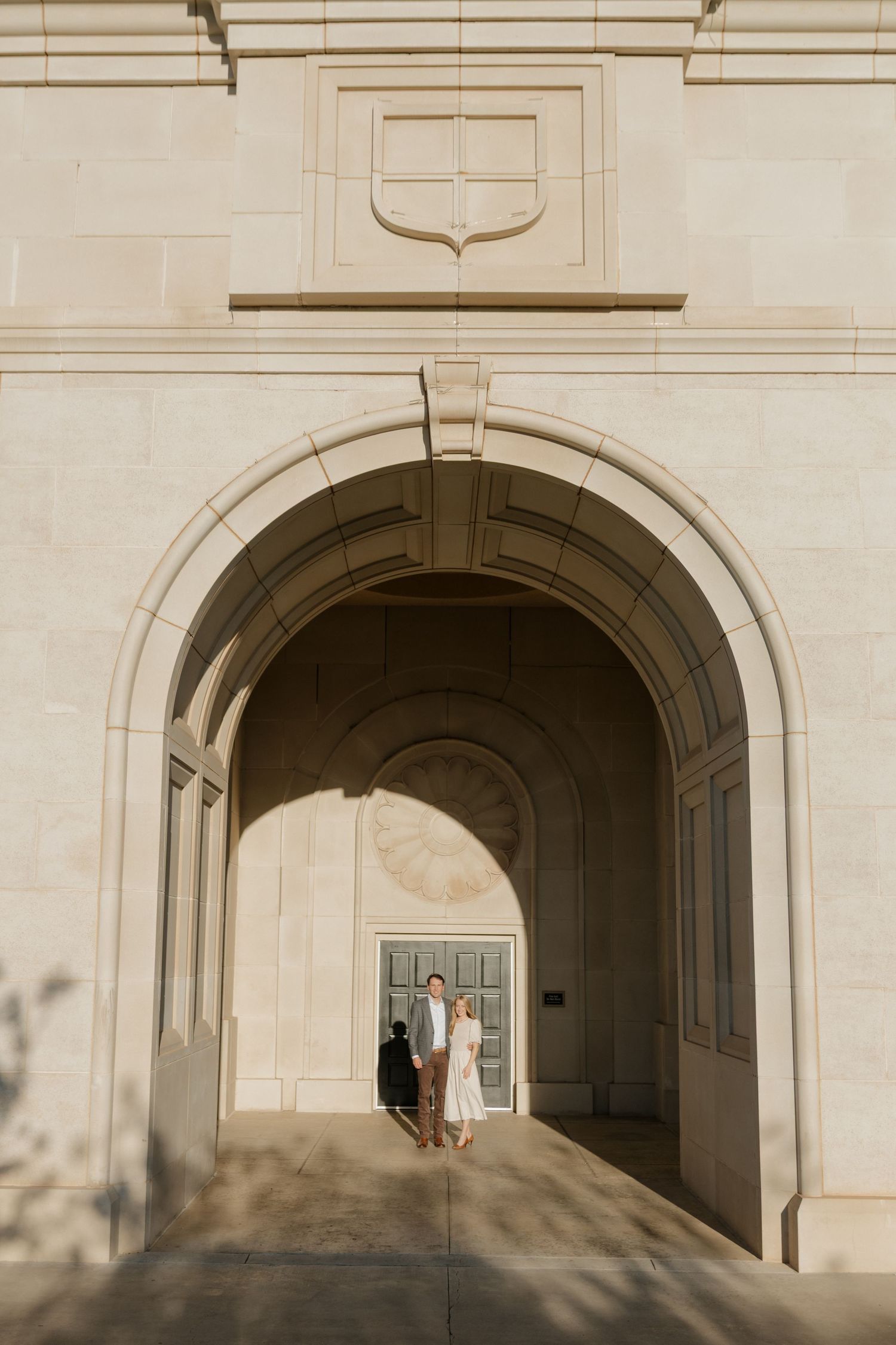 Elegant archway entrance of a stone building with dappled shadows and a couple standing in the doorway.