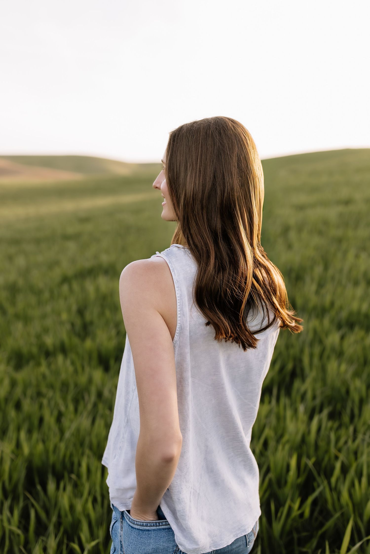 Person wearing white sleeveless top standing among tall green wheat stalks.