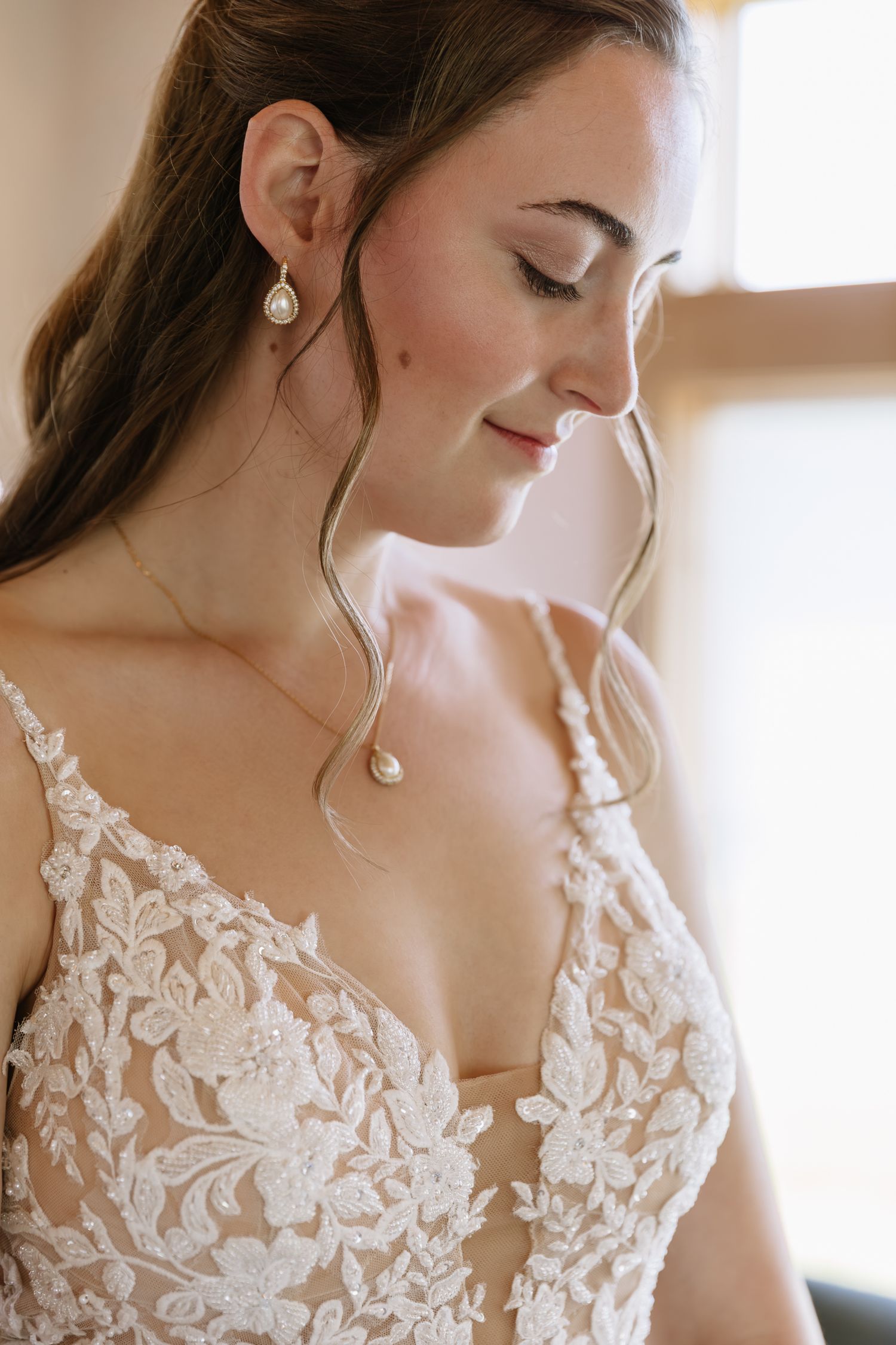 Close-up details of delicate white lace floral appliques on a wedding dress bodice with pearl drop earrings.