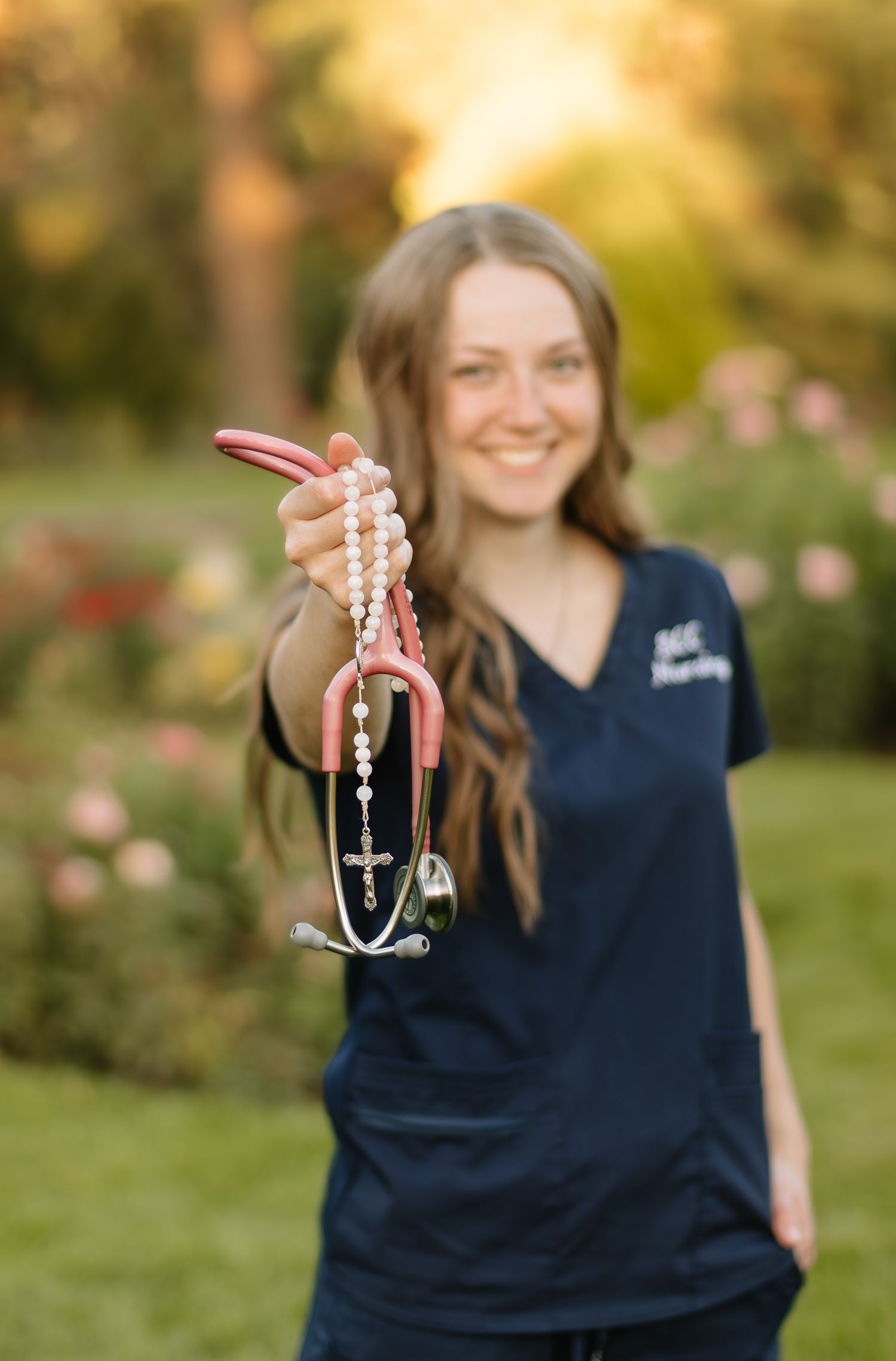 A person in a navy blue shirt holds up decorative cross necklaces in a sunny outdoor garden setting.