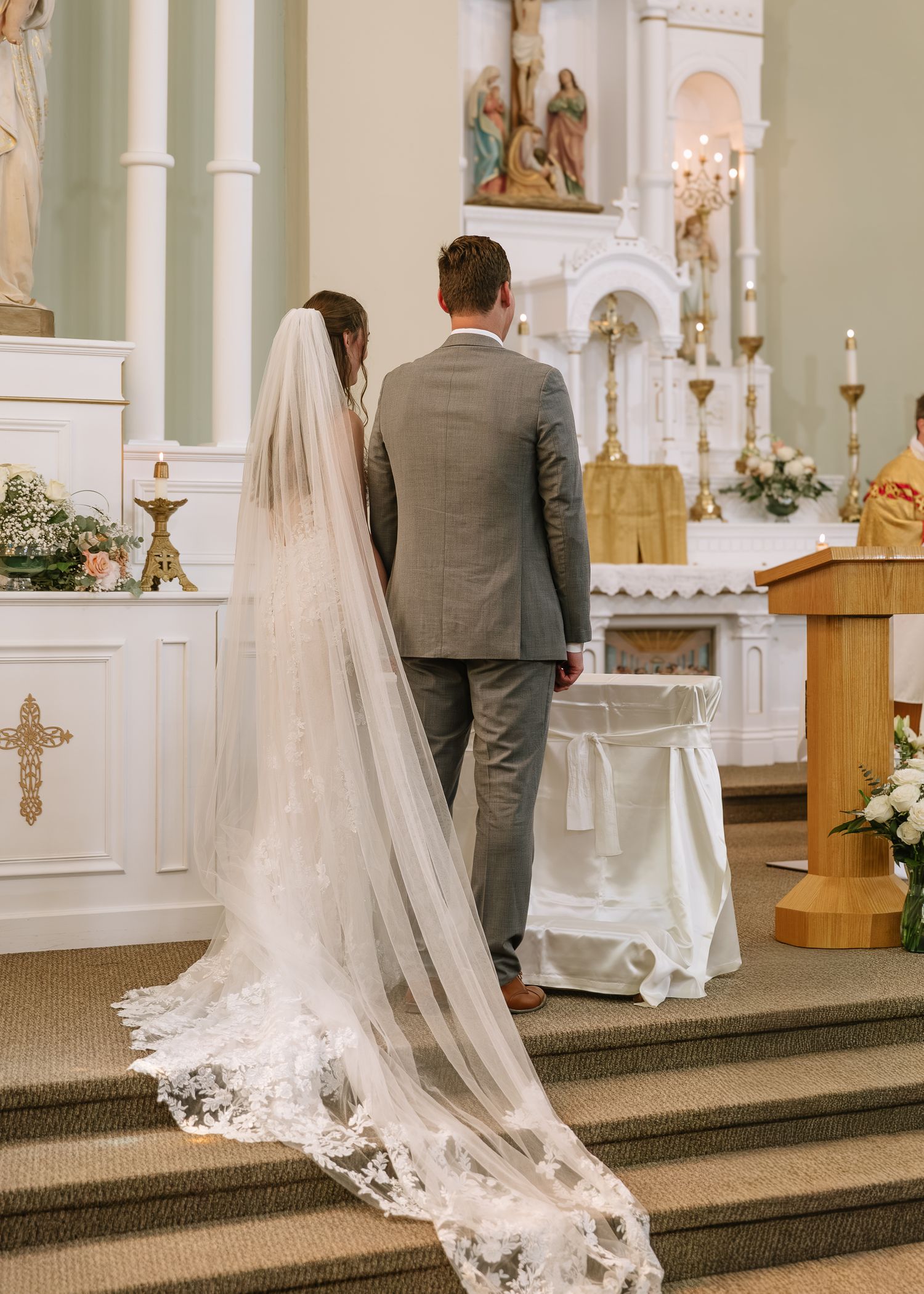 A bride and groom stand at the altar during their wedding ceremony in an elegant church with white floral decorations.