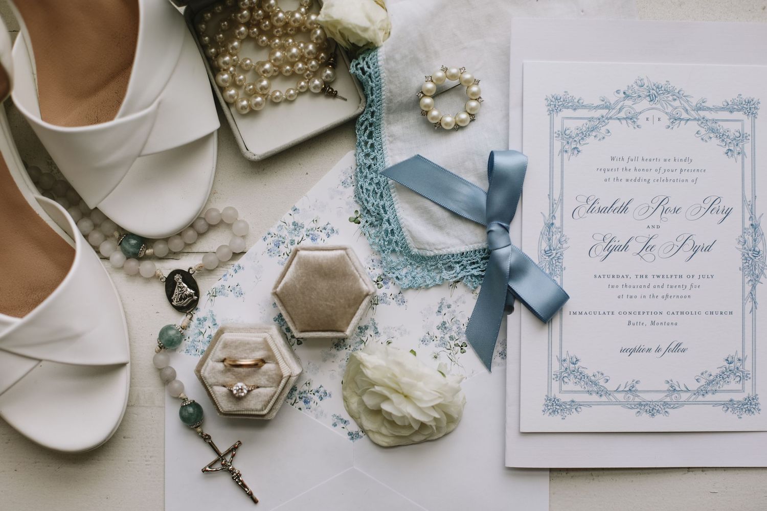 Wedding accessories including invitation, shoes, jewelry and religious items arranged on white background.