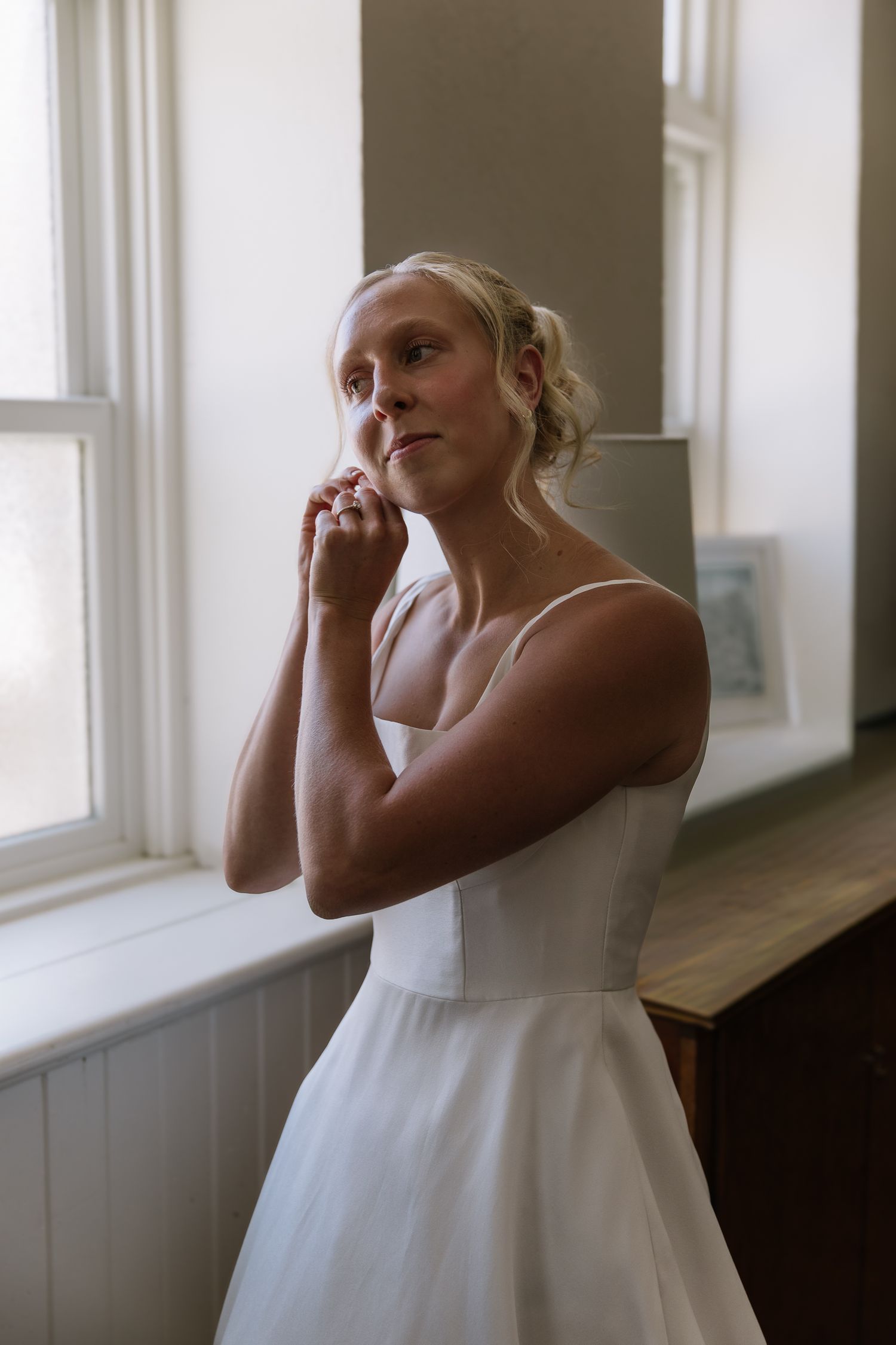 A series of four soft-focus photos showing someone in a white dress by a window in natural light.