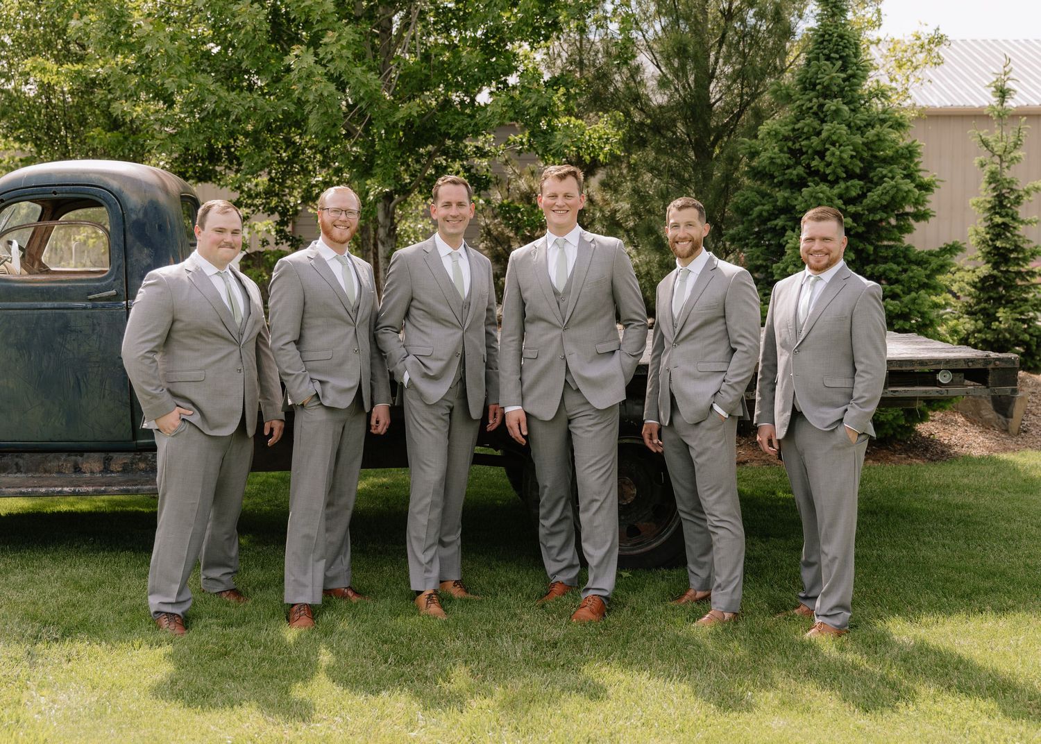Wedding party wearing matching gray suits and red socks poses playfully on grass for creative group photo.