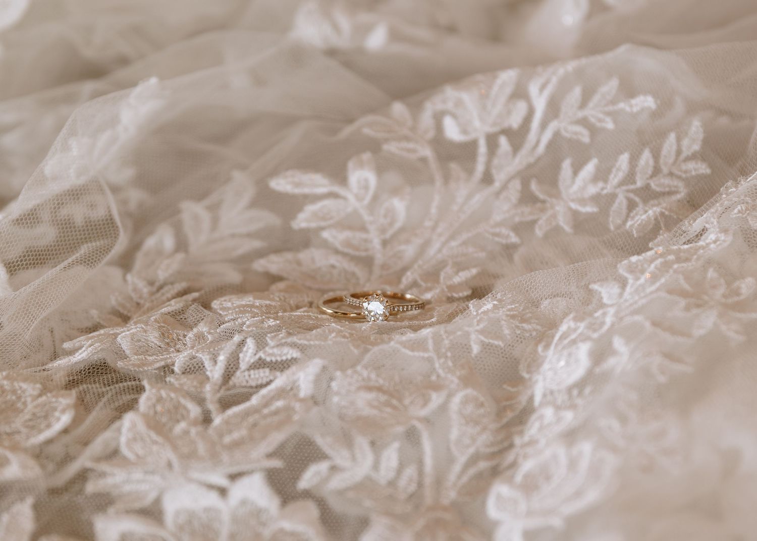 A delicate lace wedding dress fabric with intricate floral patterns and embroidered details lies on a soft surface.