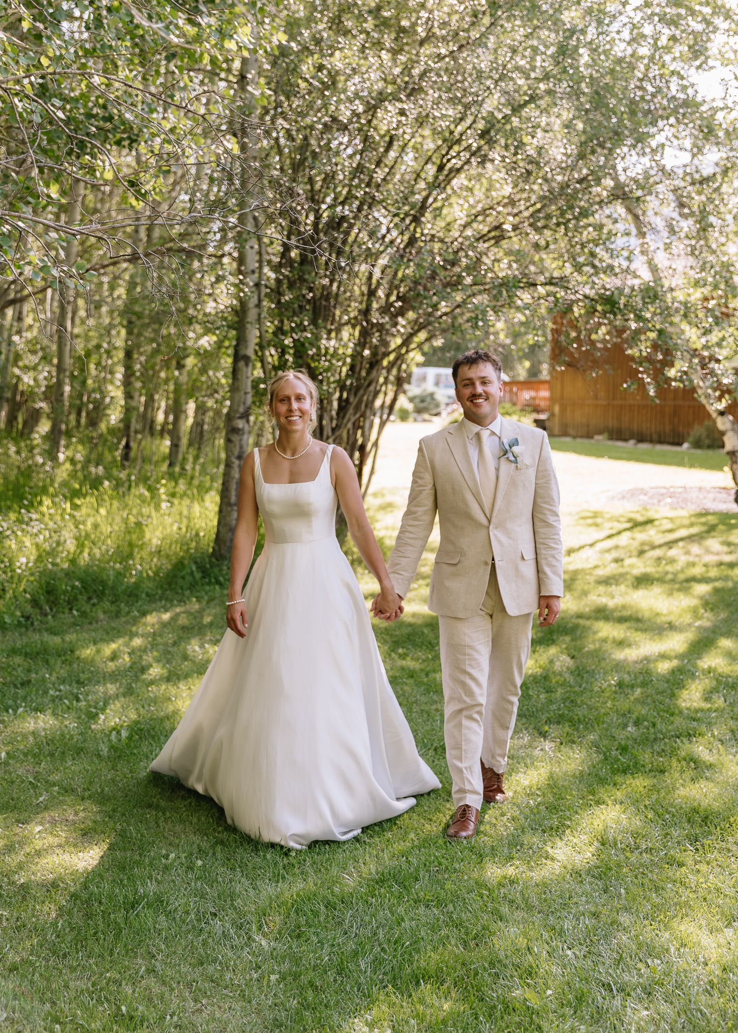 A couple walks together through a sunlit garden pathway with trees creating a natural archway above.