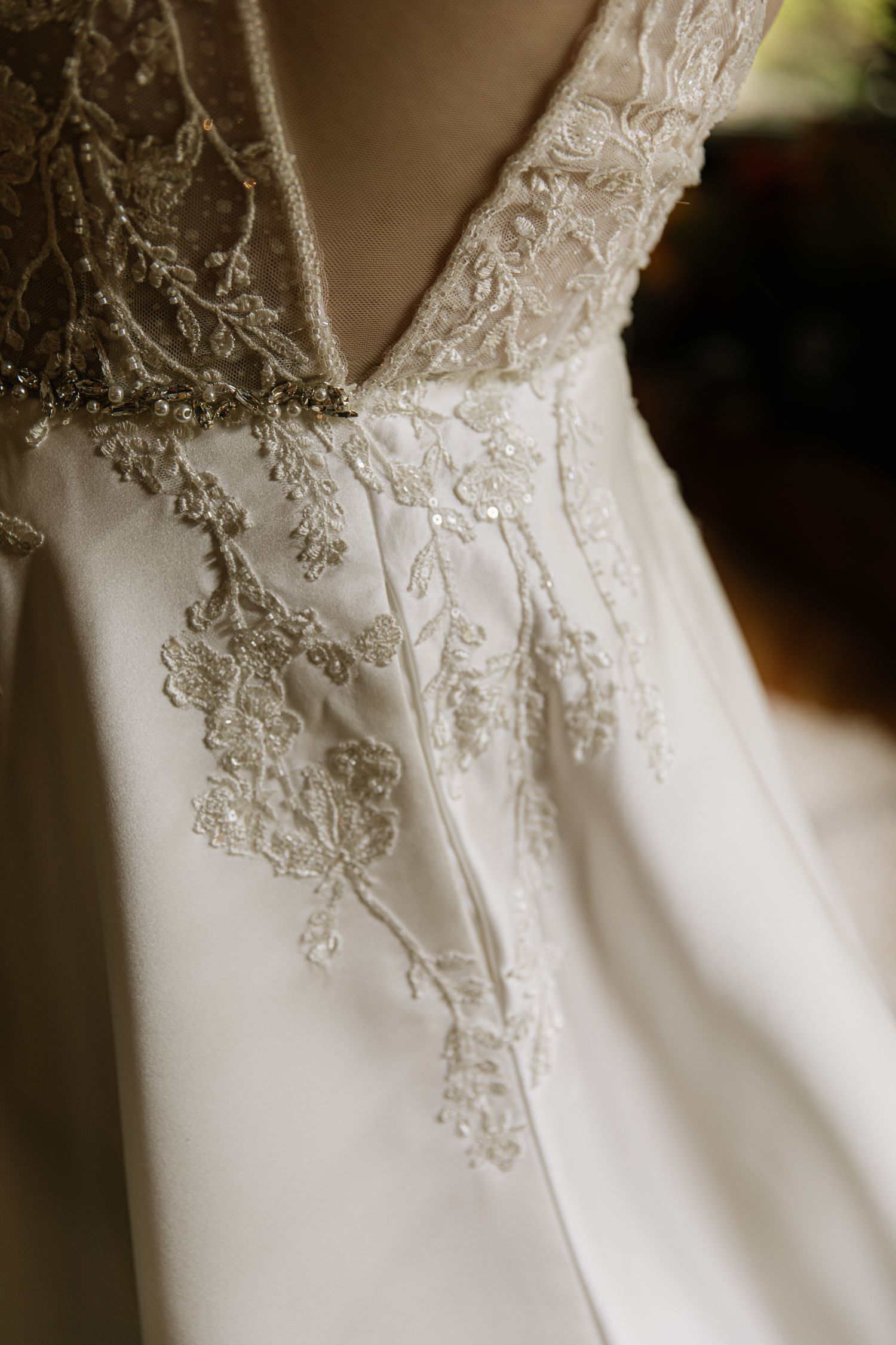 Close-up detail of delicate lace embroidery and beadwork on a white wedding dress bodice.