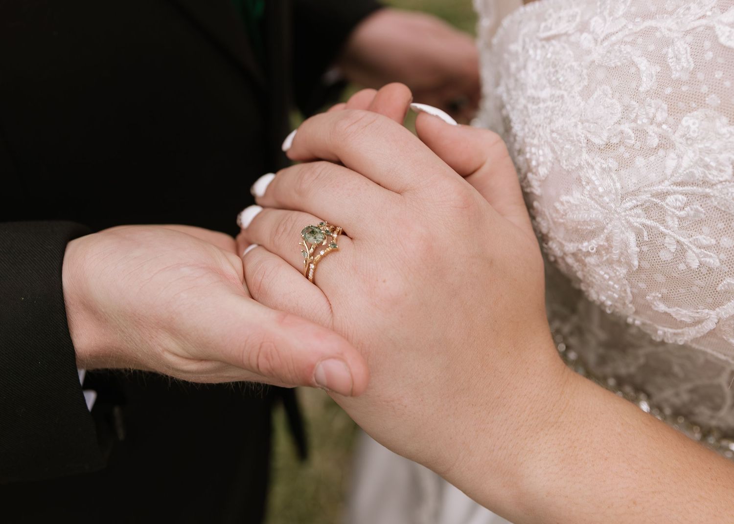 Close-up of hands clasped together with a sparkling engagement ring visible on white lace background.