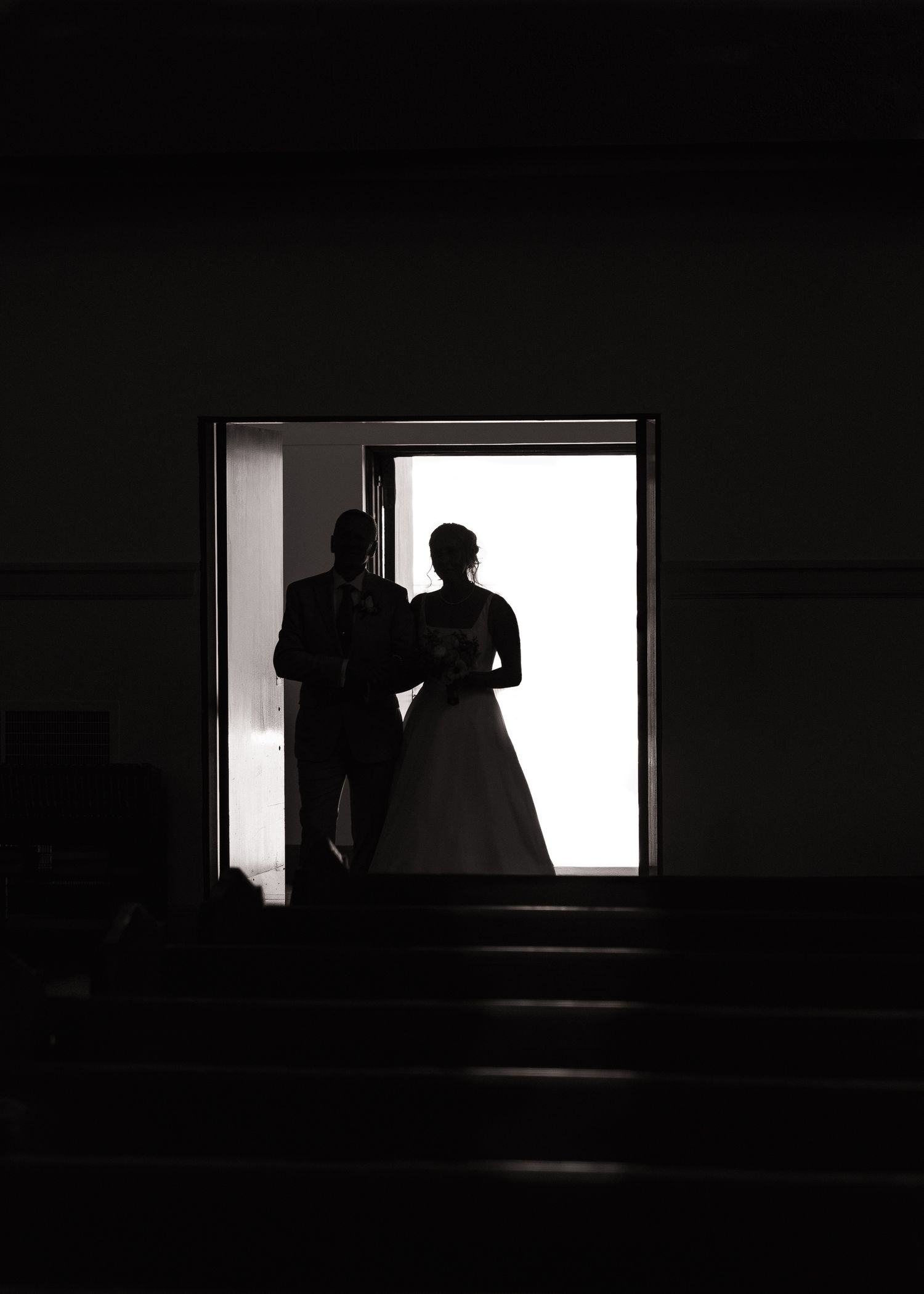 A silhouetted figure stands in a dark room against a bright window creating a dramatic contrast.