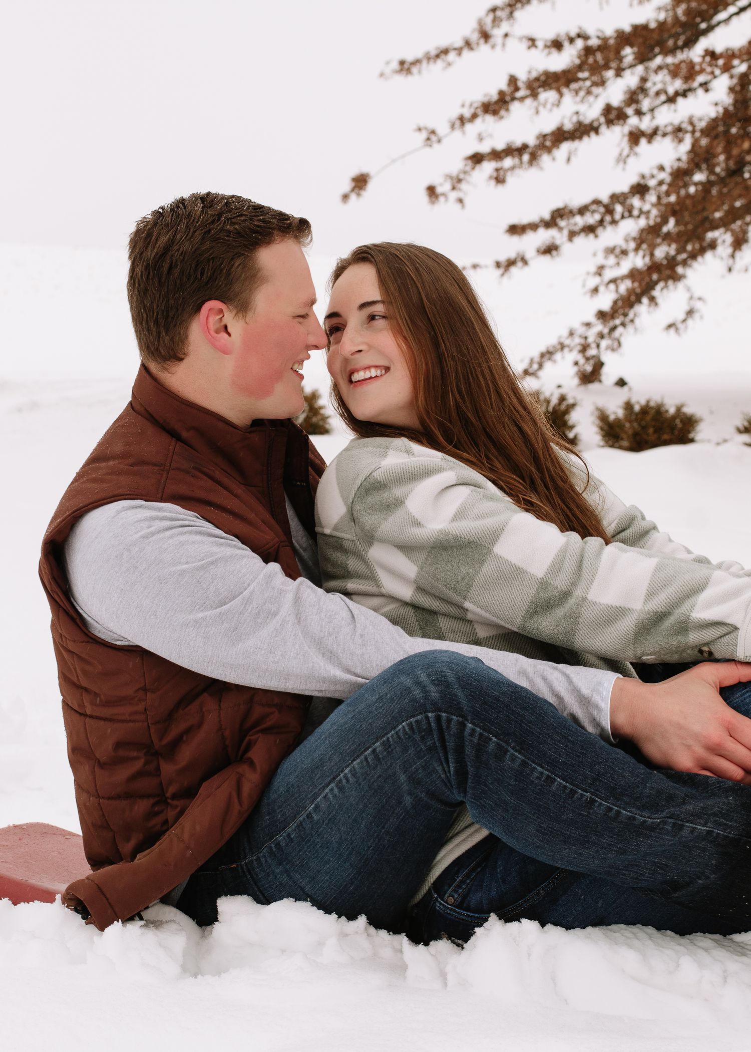 A couple in winter attire lying in the snow sharing an intimate moment during a romantic outdoor photoshoot.