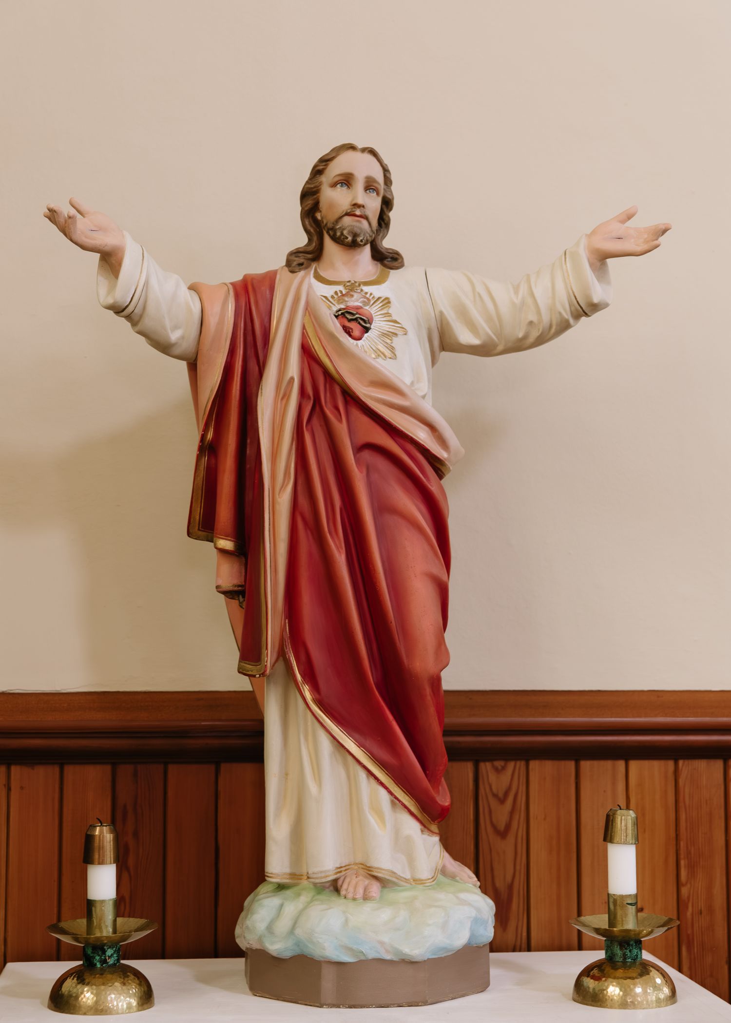 A panoramic sequence of a Jesus statue with outstretched arms against a beige background with wooden paneling.