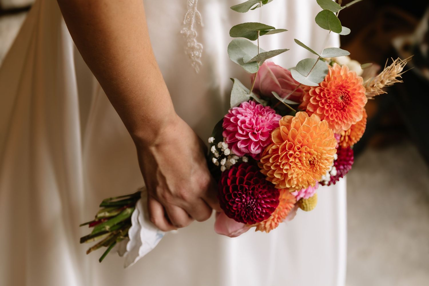 A series of hands holding vibrant dahlia bouquets in warm orange, pink and red tones against a light background.