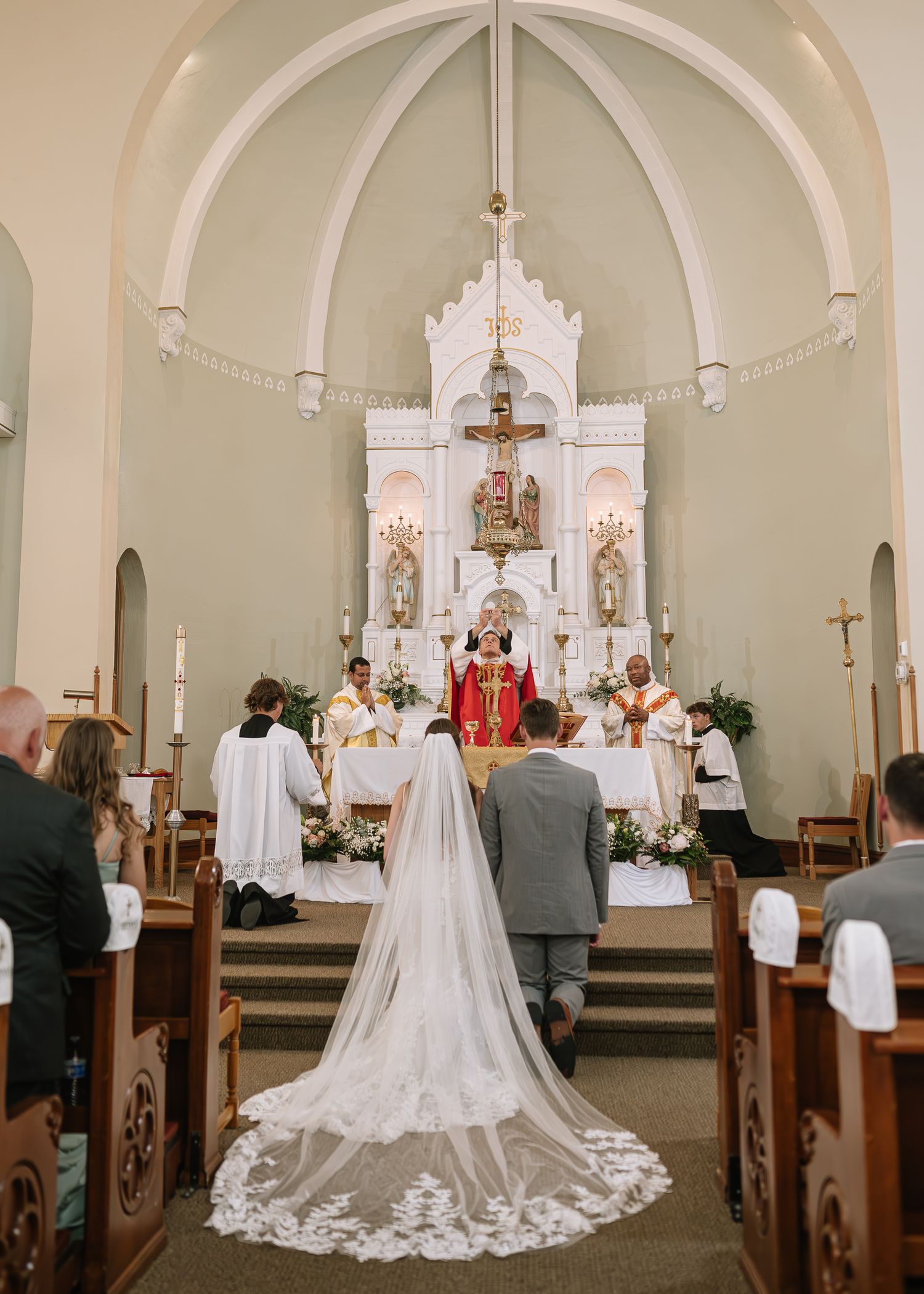 A traditional Catholic church wedding ceremony with a long white lace train trailing down the aisle.