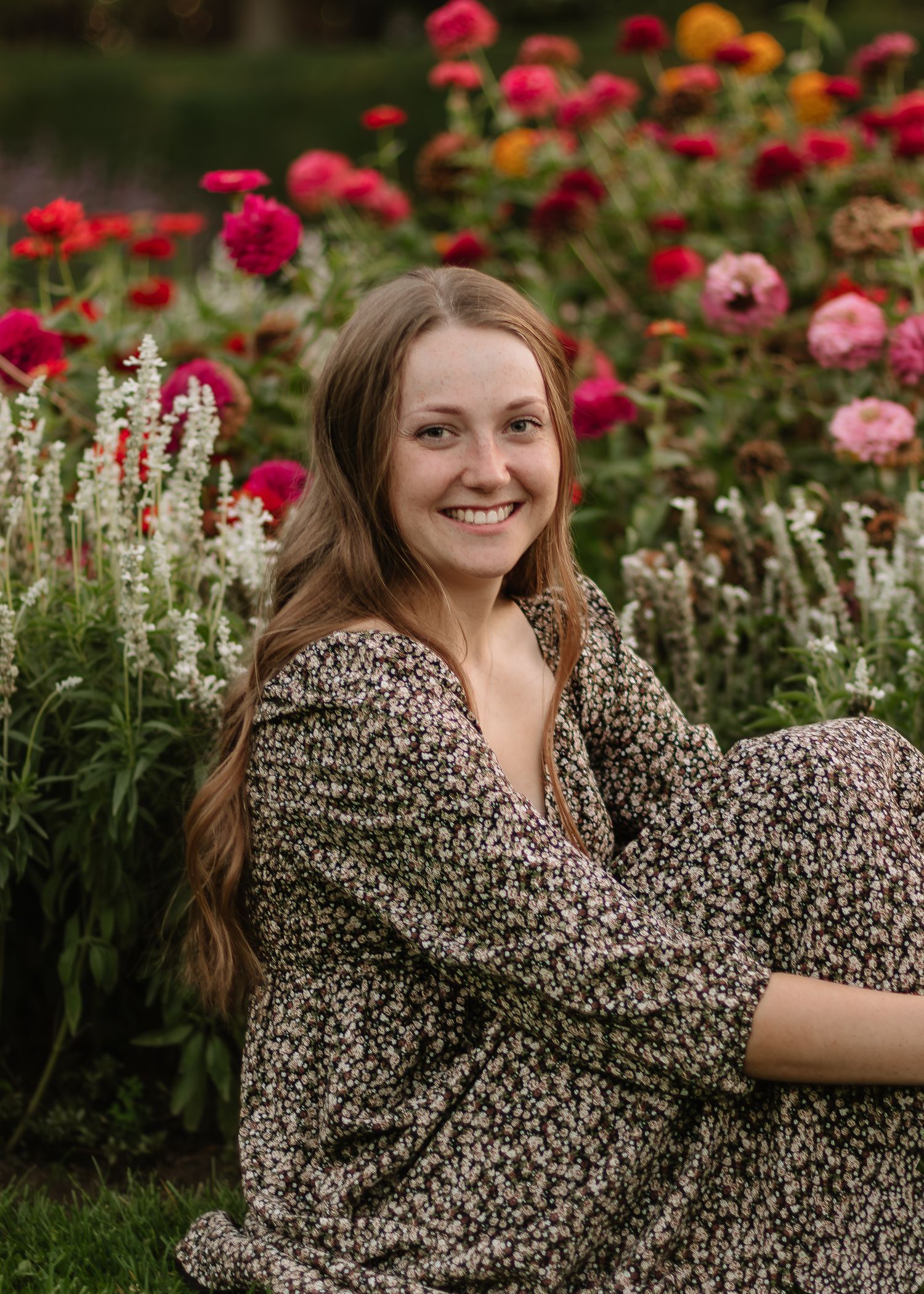 A person in a floral print dress poses in a garden filled with vibrant pink and red flowers.
