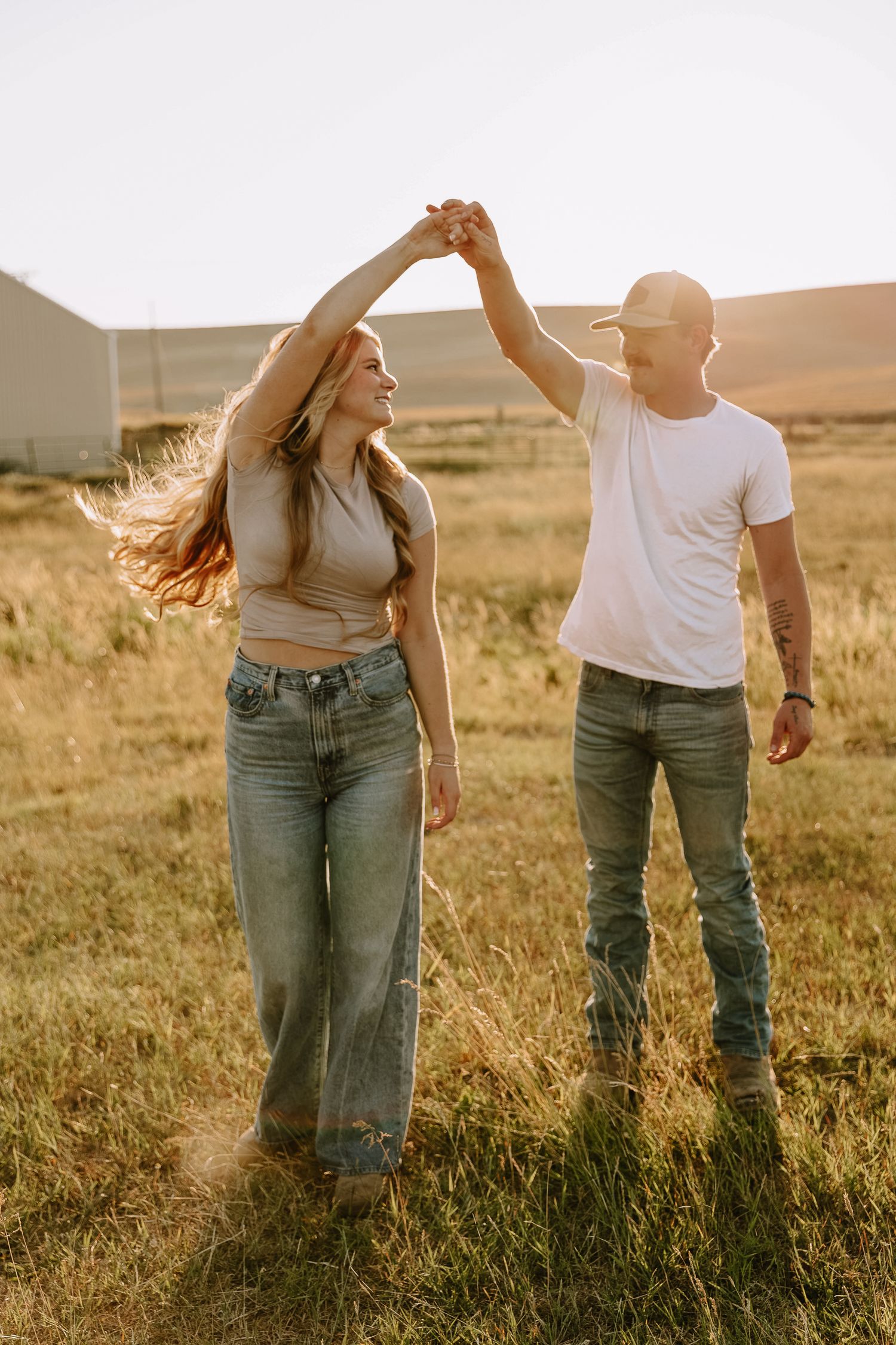 A couple dancing together in a golden field at sunset wearing casual jeans and white tops.