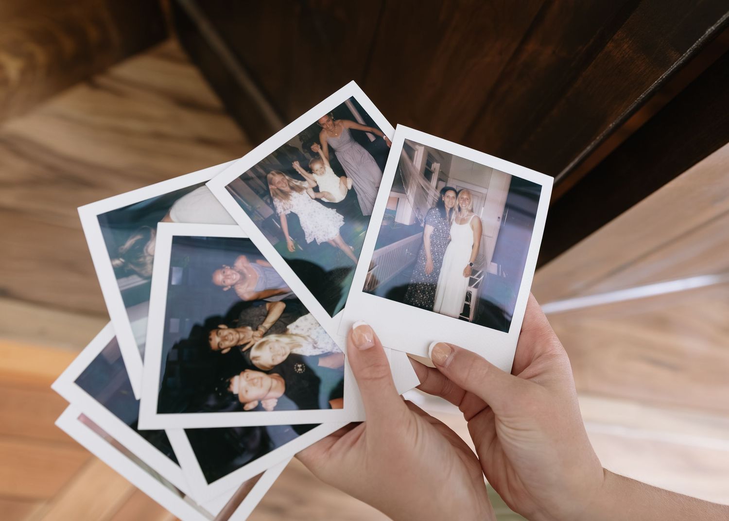 A person's hands arranging and looking through a collection of Polaroid photographs spread out on a wooden surface.
