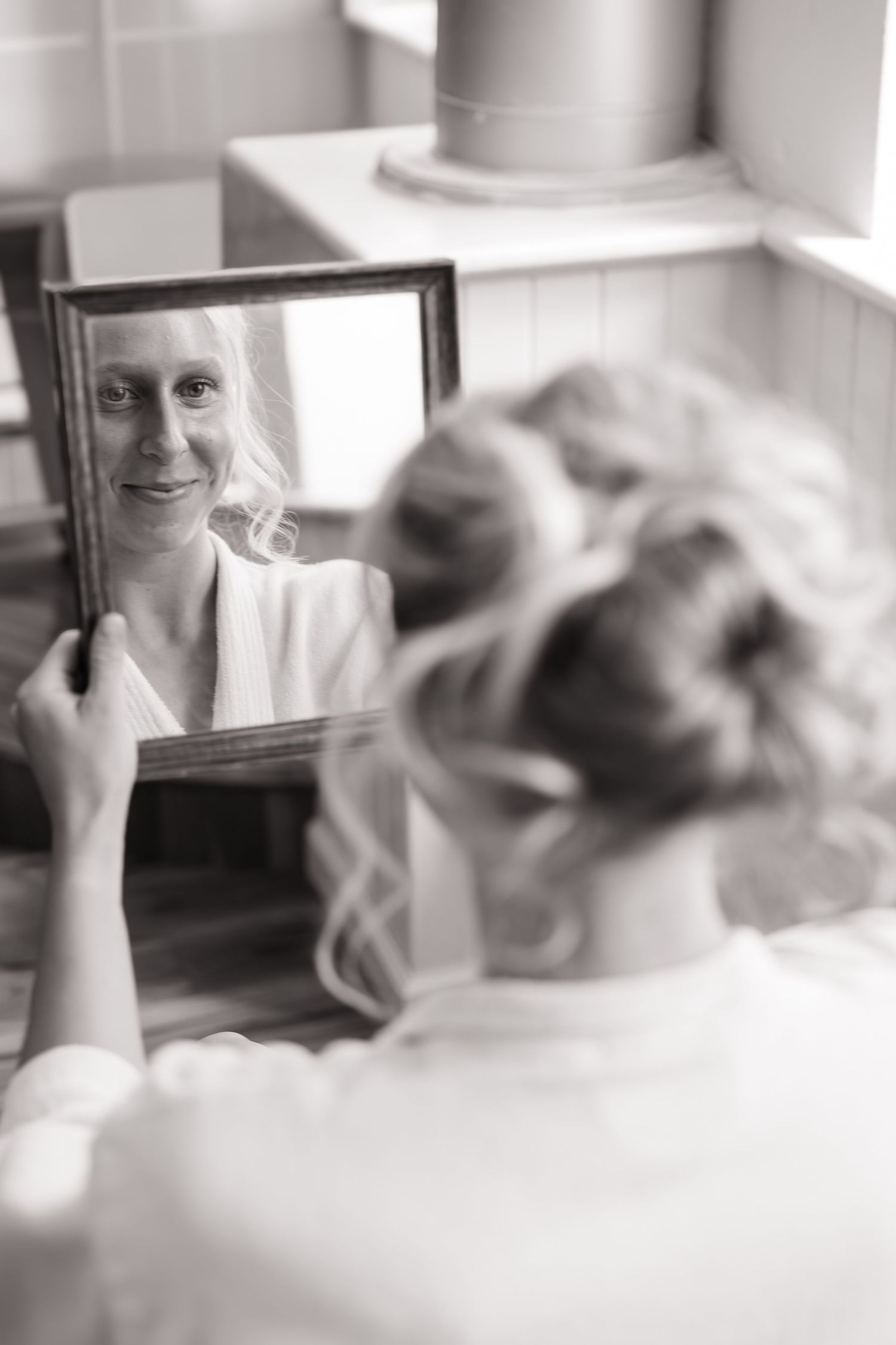 Black and white photo of wedding preparation reflected in mirror.