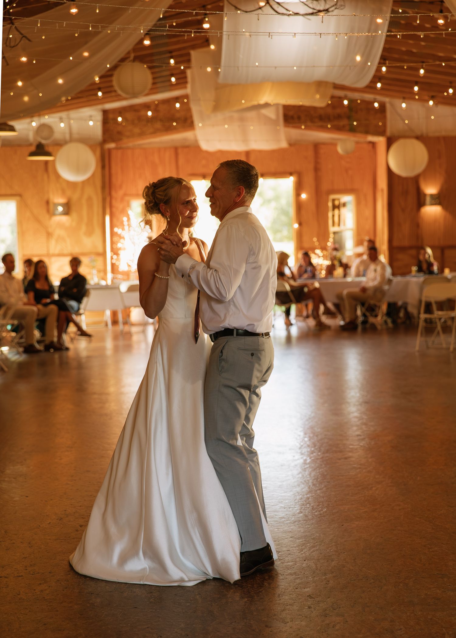 A couple dances together in a spacious ballroom decorated with twinkling lights and white paper lanterns.