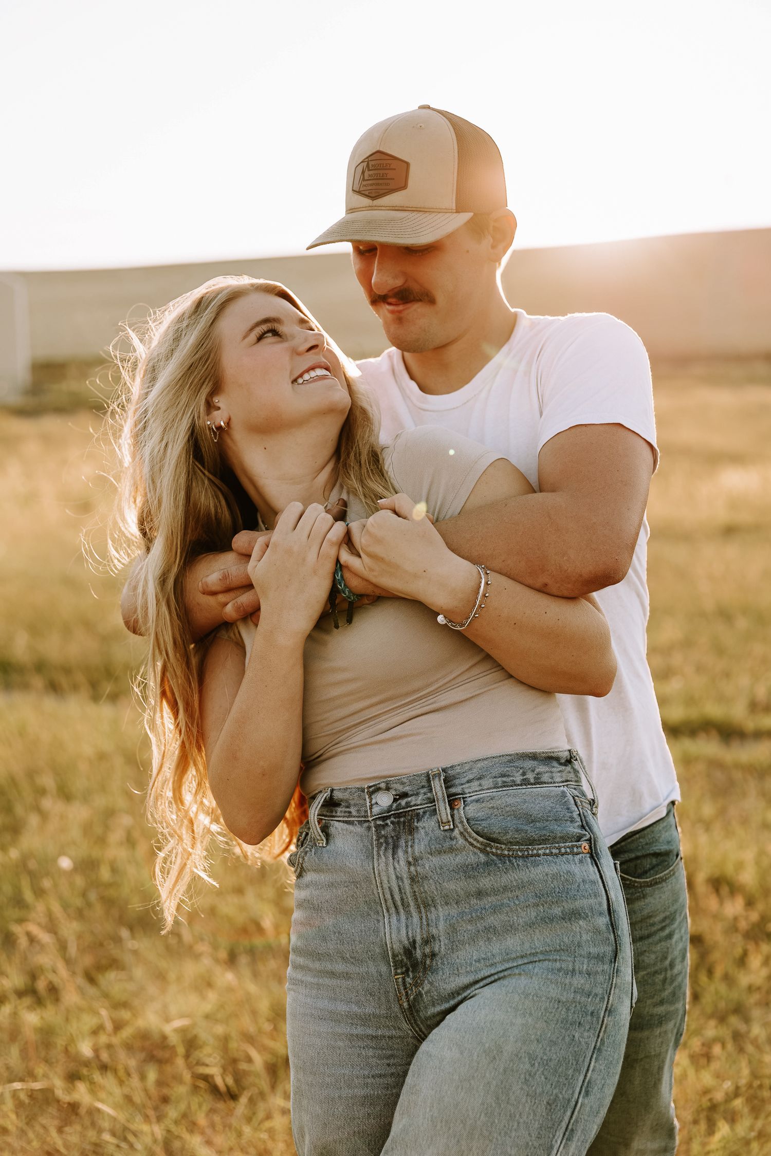A romantic couple embraces in a golden sunlit field during sunset, creating an intimate moment in nature.