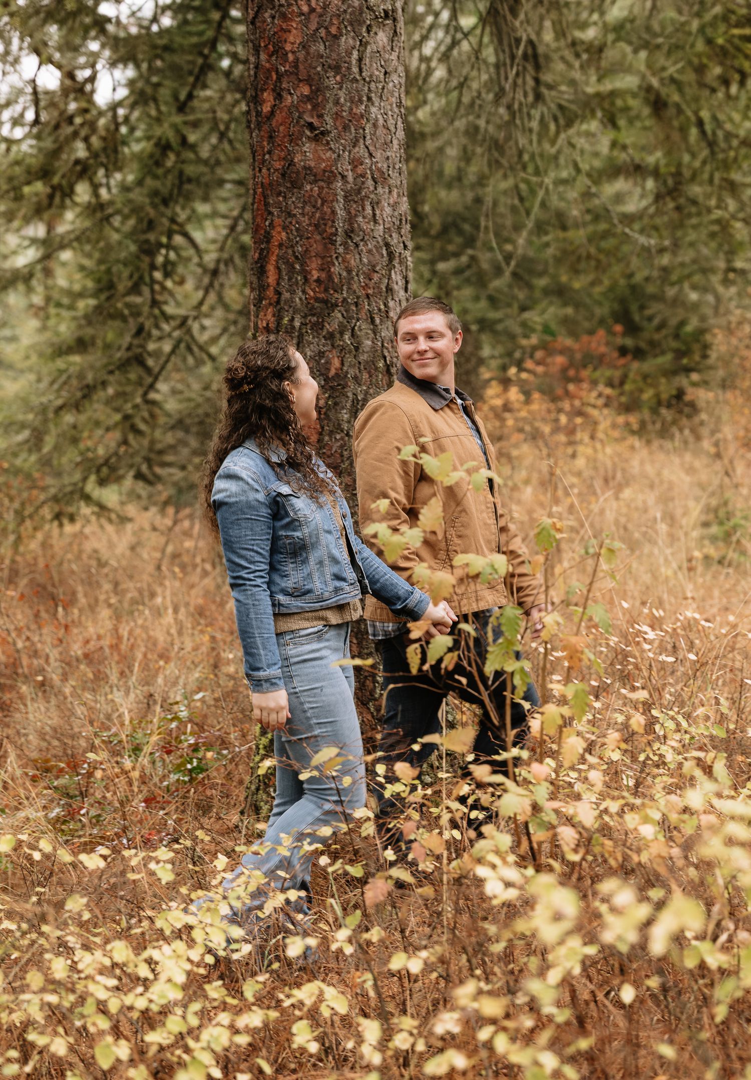 Person in denim jacket poses against large tree trunk in autumn forest setting with golden foliage.