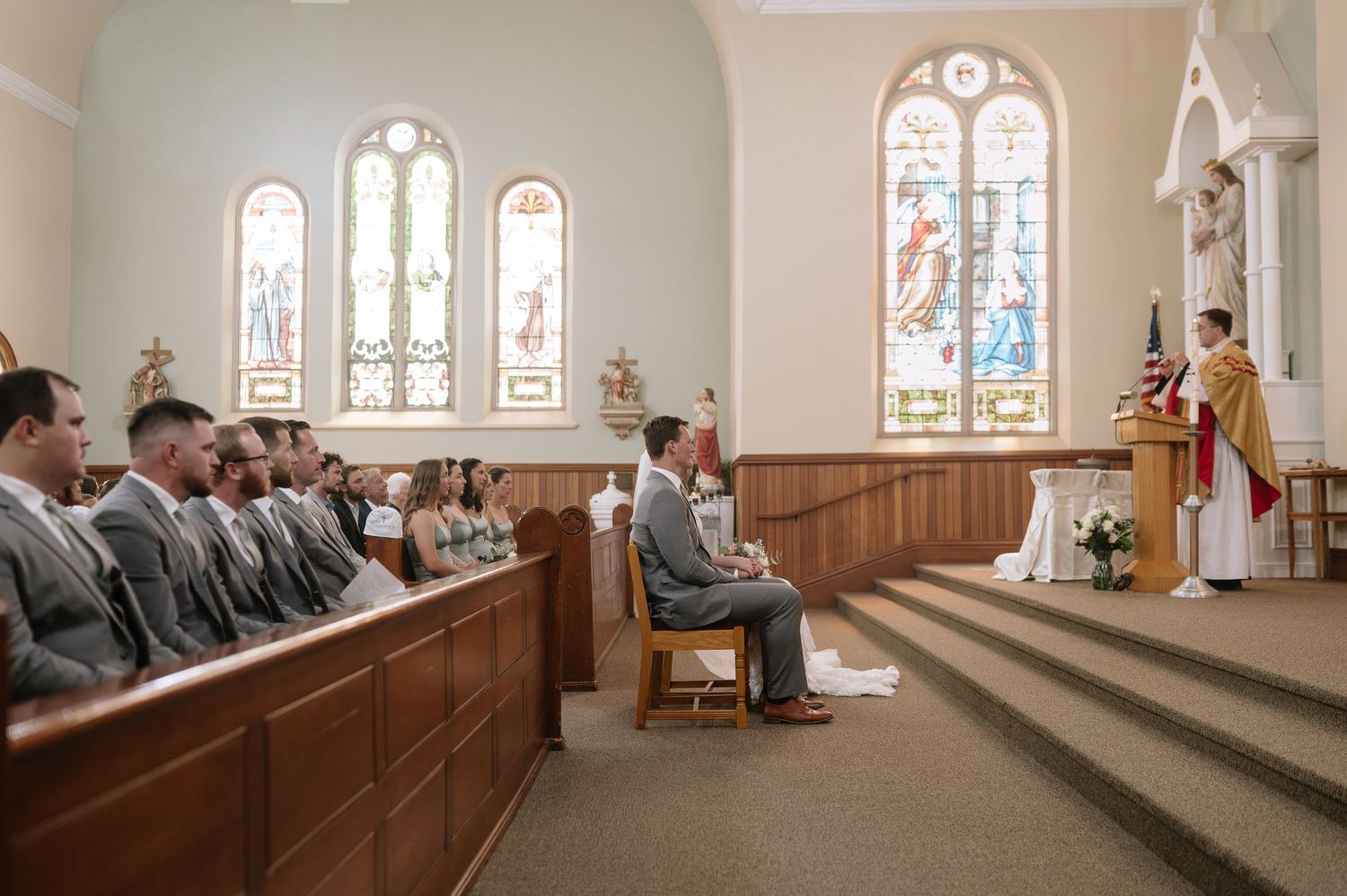 Interior view of a church sanctuary with stained glass windows and wooden pews during a ceremony.