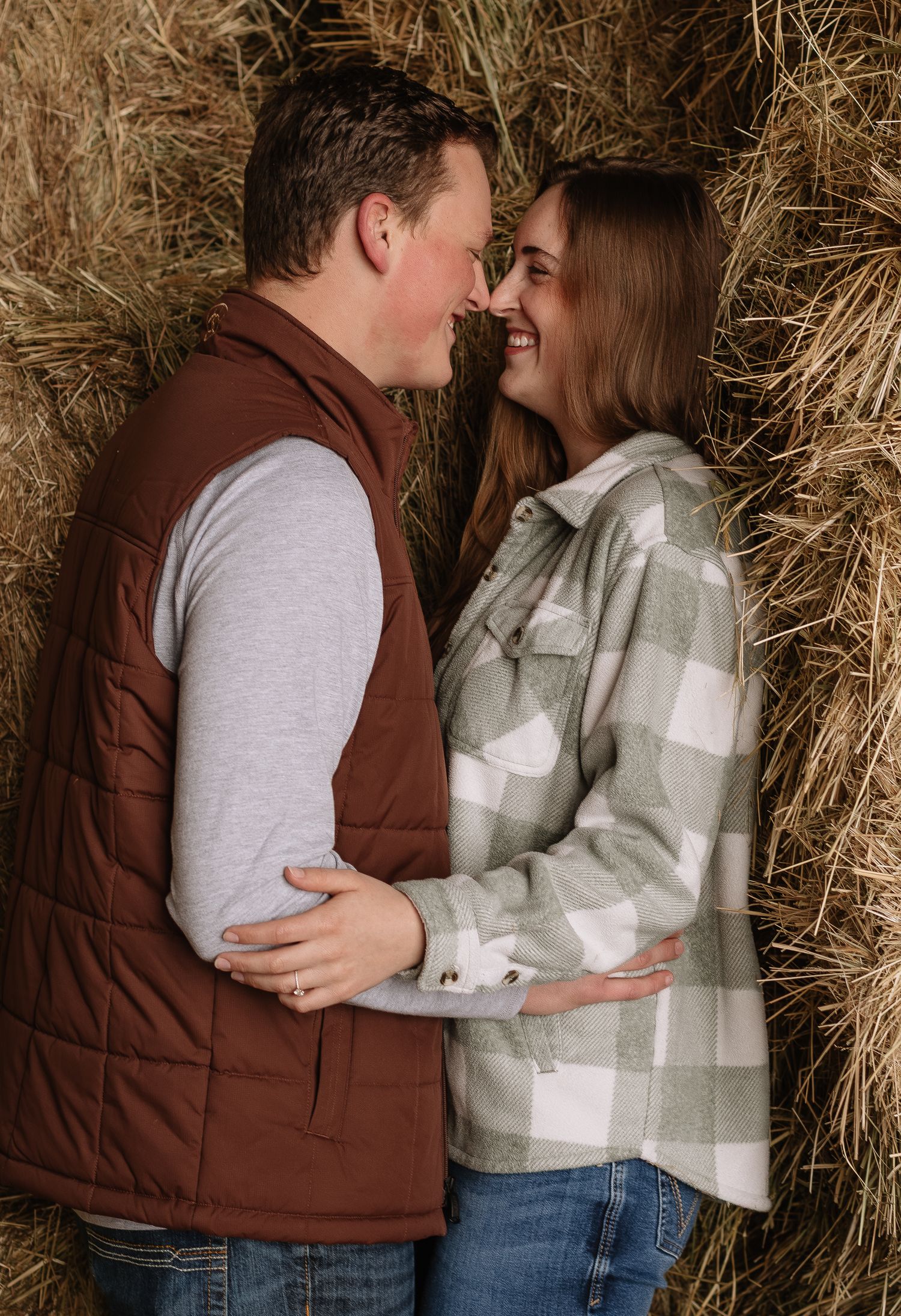Romantic couple embraces in rustic barn setting with hay bales creating warm autumn atmosphere.