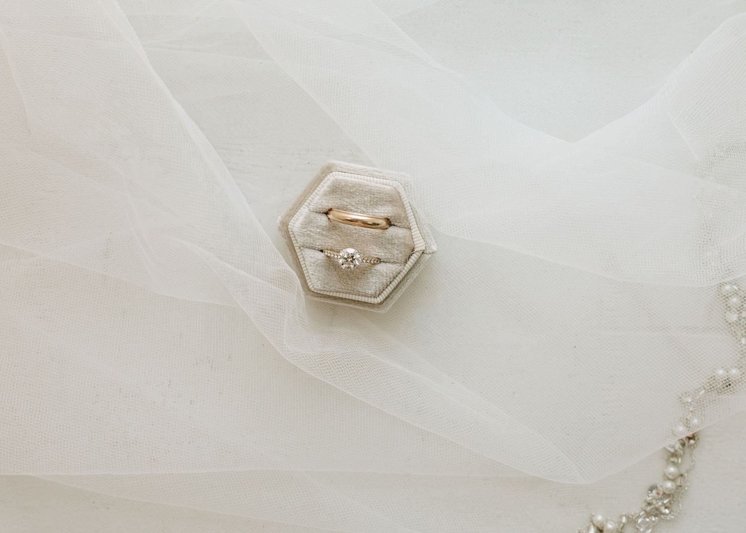 Two gold wedding rings rest inside a hexagonal white ring box on delicate sheer fabric.