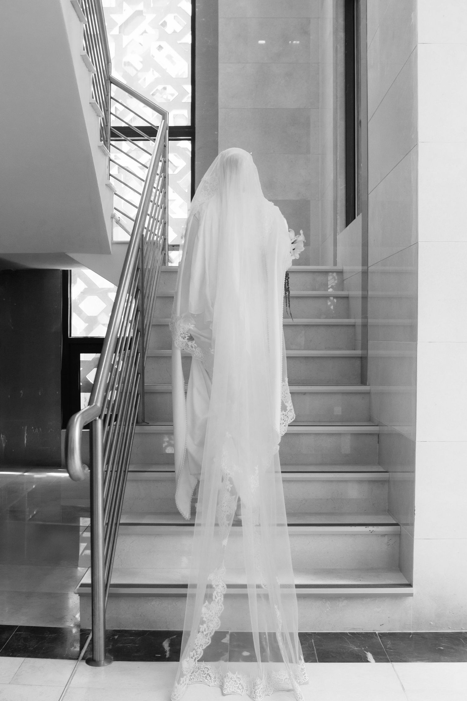A ghostly figure in a flowing white veil stands mysteriously on a modern staircase in black and white photography.
