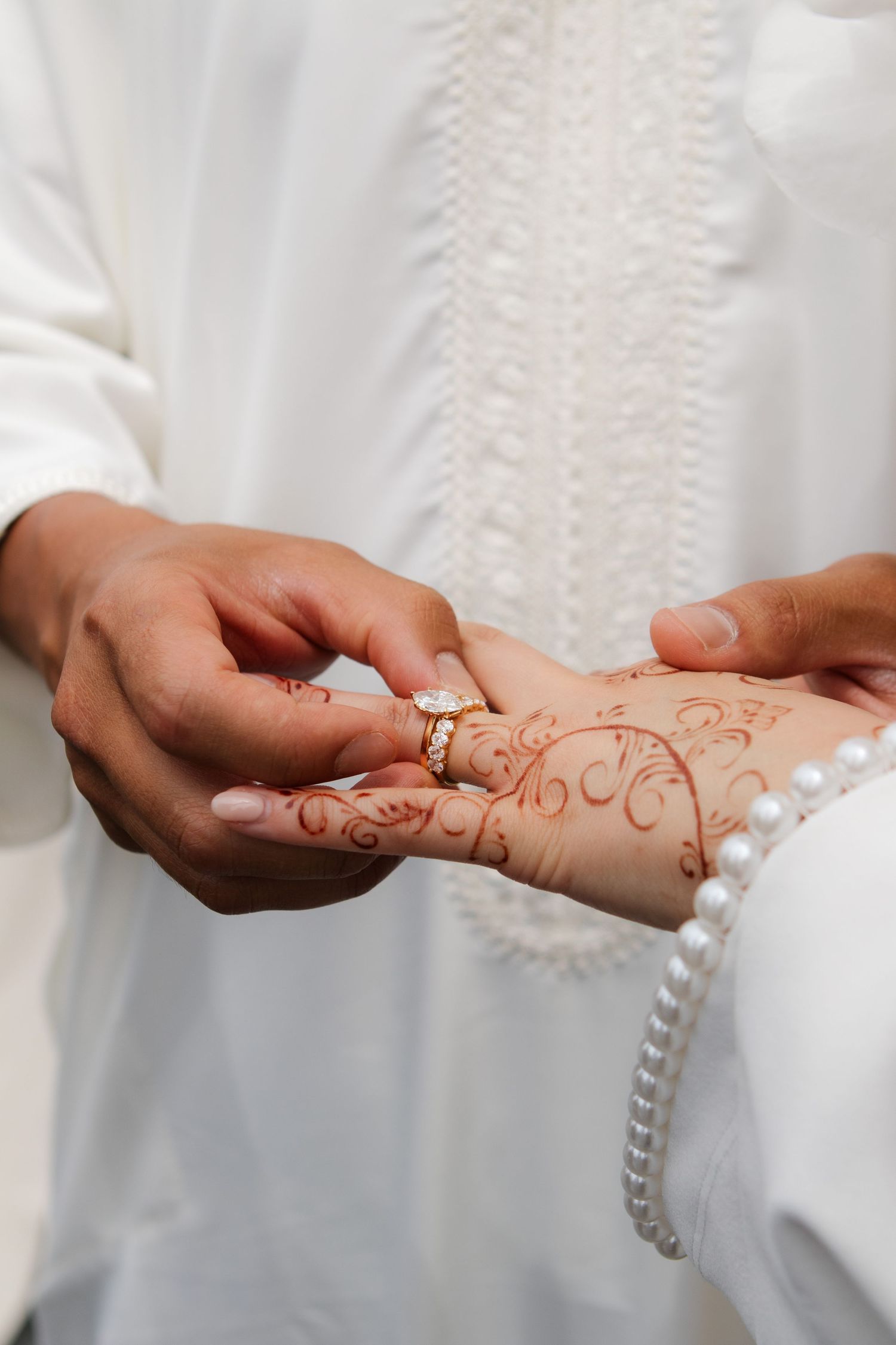 A close-up of hands exchanging a wedding ring, with intricate henna designs visible on one hand.
