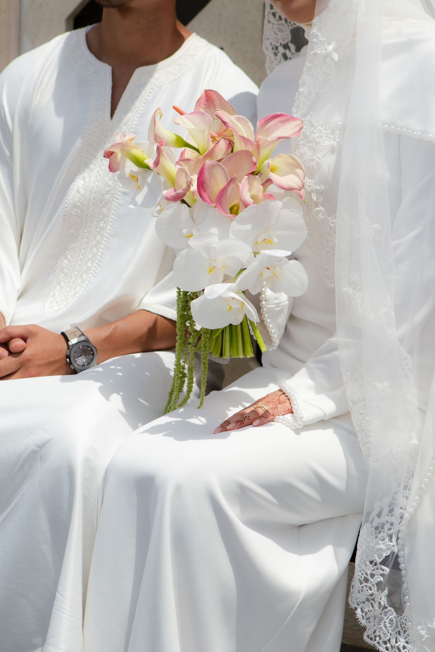 A wedding party wearing white attire holds delicate pink and white orchid bouquets against a light background.