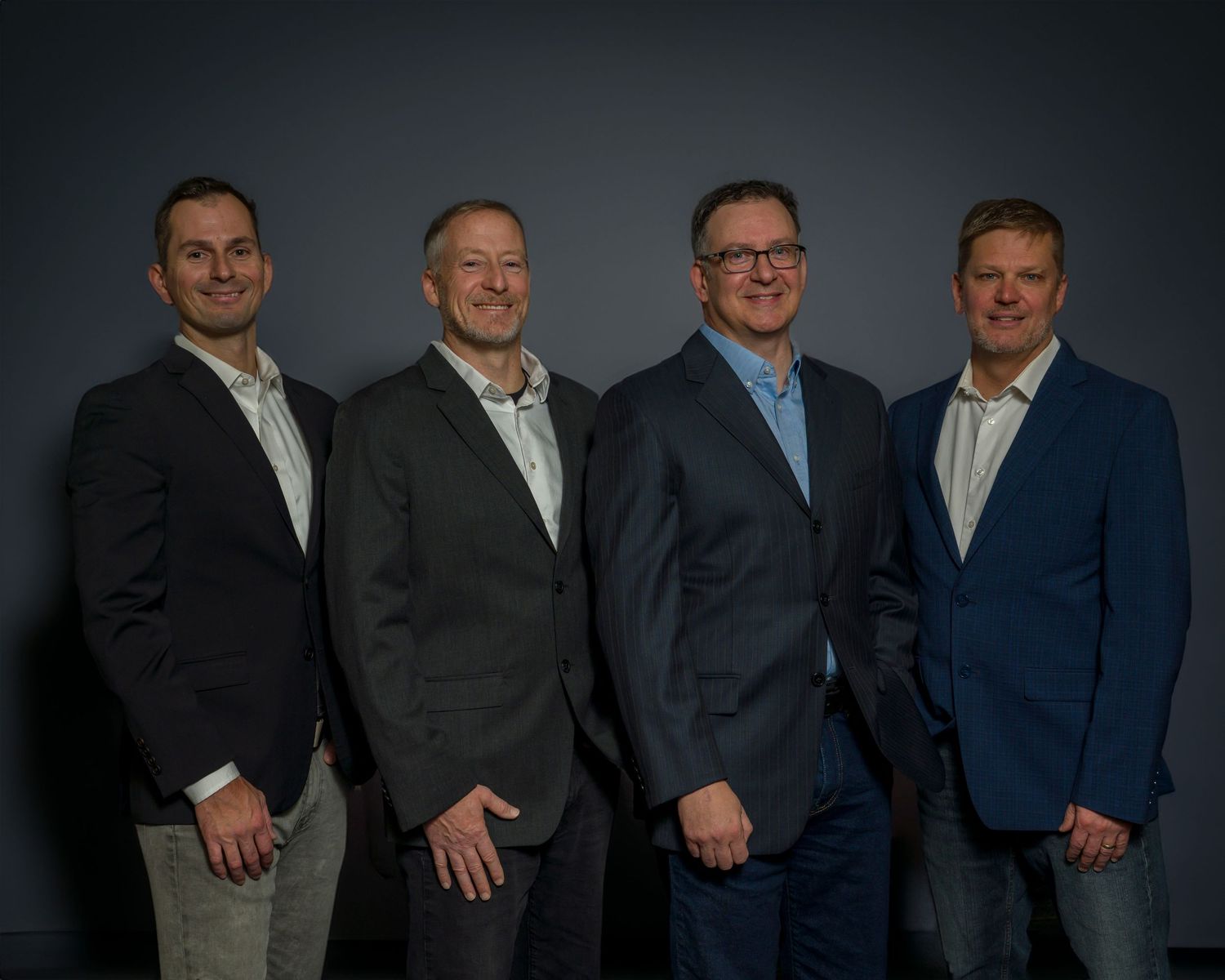 Business team members photographed in formal attire against muted gray studio background.