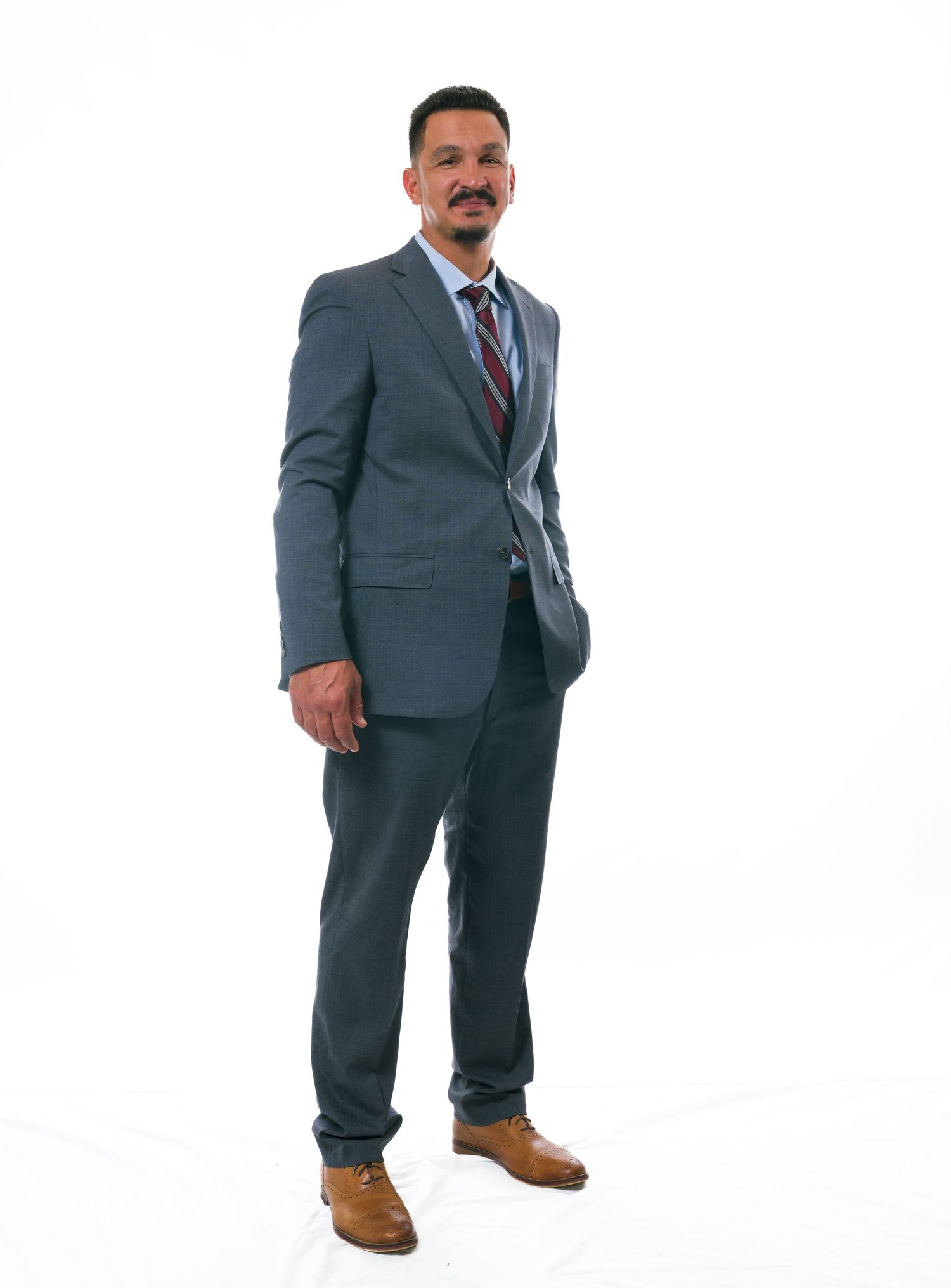 Professional in a charcoal gray business suit and striped tie stands confidently against white background.