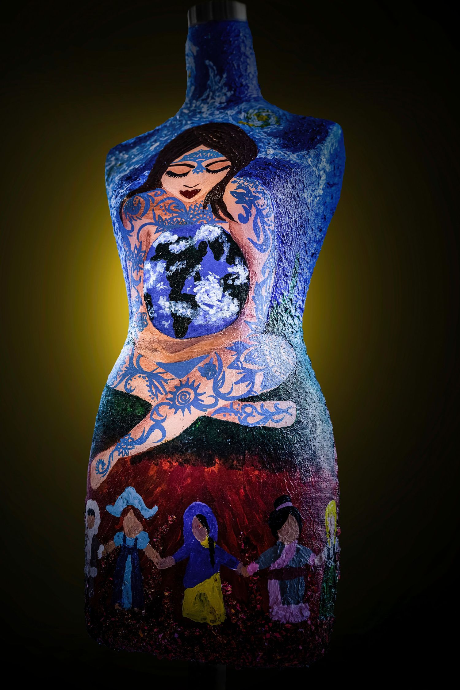 Illuminated artistic mannequin torso with painted fantasy design featuring Earth and mystical figures on dark background.
