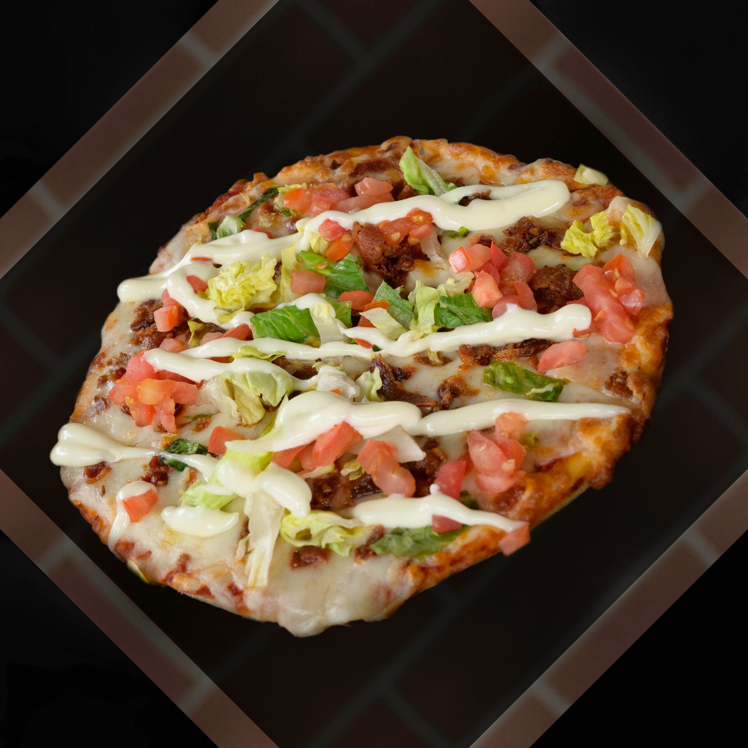 An oval flatbread pizza topped with shredded lettuce, diced tomatoes, and drizzled with creamy white sauce on a dark surface.